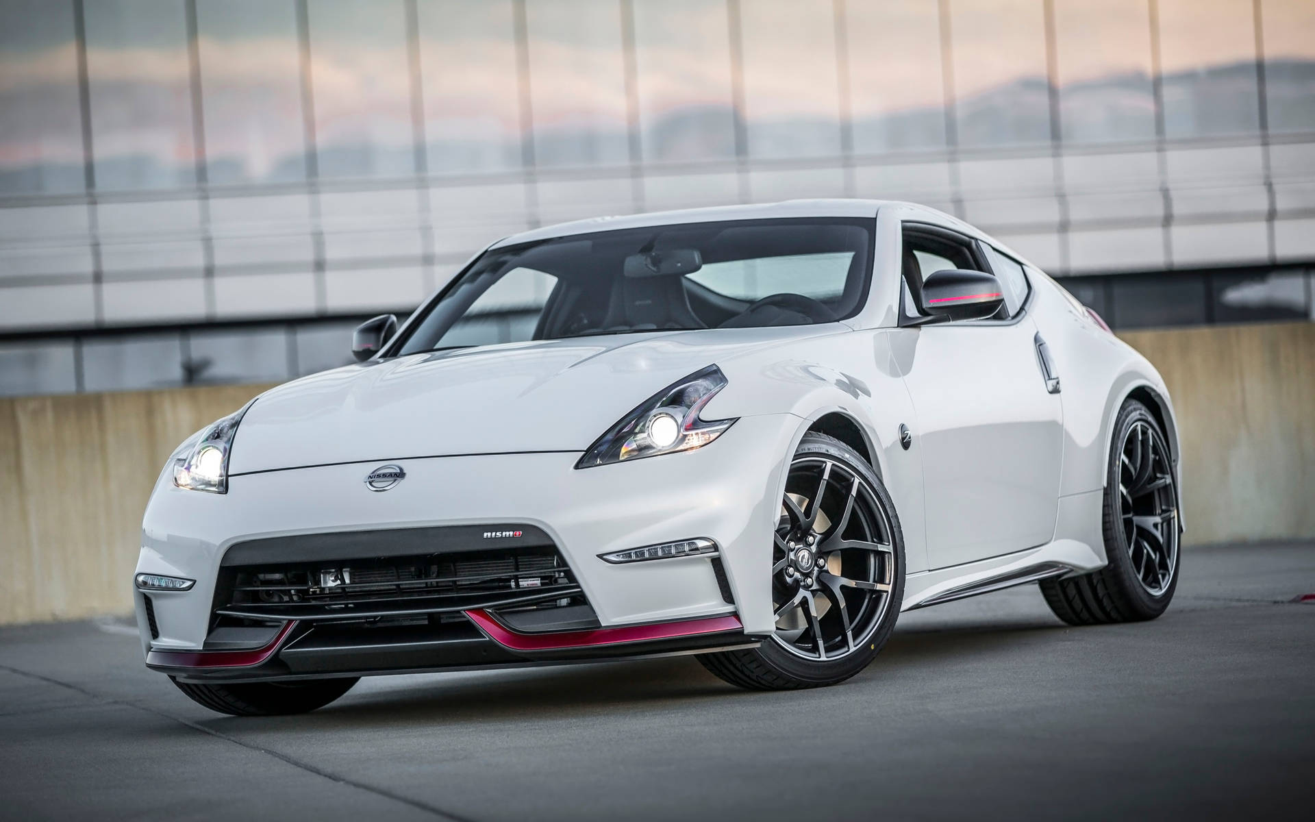 白色日產370Z跑車帶紅色點綴，停泊在黃昏時分的玻璃建築前。
