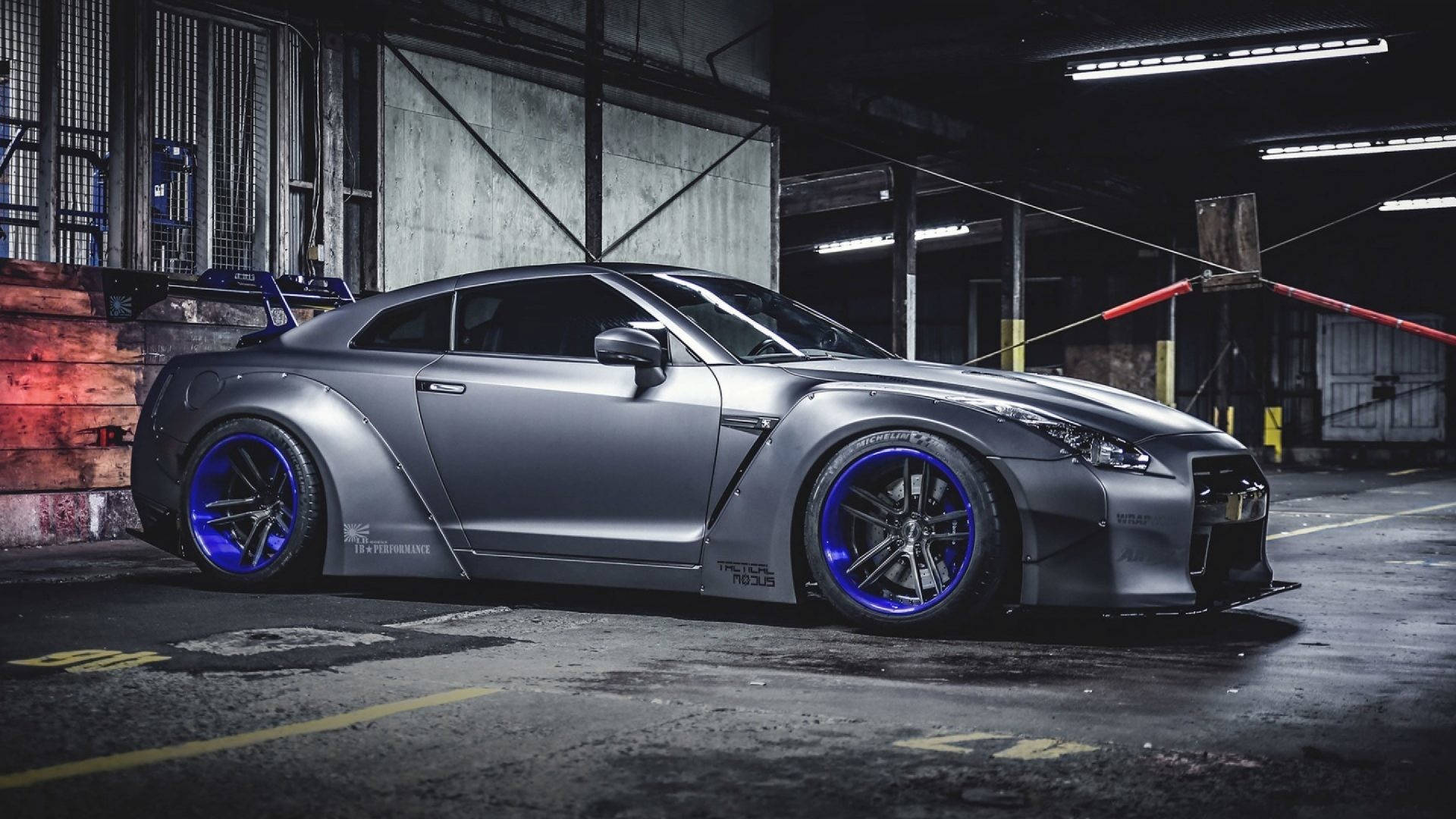 尼桑GT-R 定製車身套件 壁紙 — 一架啞光灰色日產GT-R，配以發光藍色輪圈，停泊在燈光昏暗的工業車庫內。