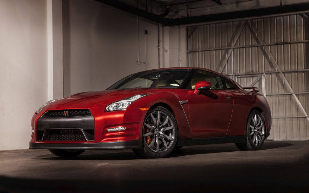 尼桑GT-R 紅櫻花漆 壁紙 — 一輛光澤的紅色日產GT-R跑車停放在一個光線昏暗的工業車庫中，車庫有混凝土牆和金屬門。