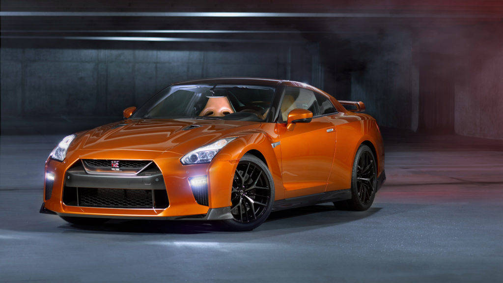 尼桑GT-R 金屬橙色車漆 壁紙 — 一輛充滿活力的橙色日產GT-R跑車在黑暗的混凝土車庫中，在戲劇性的工作室燈光下閃閃發光。