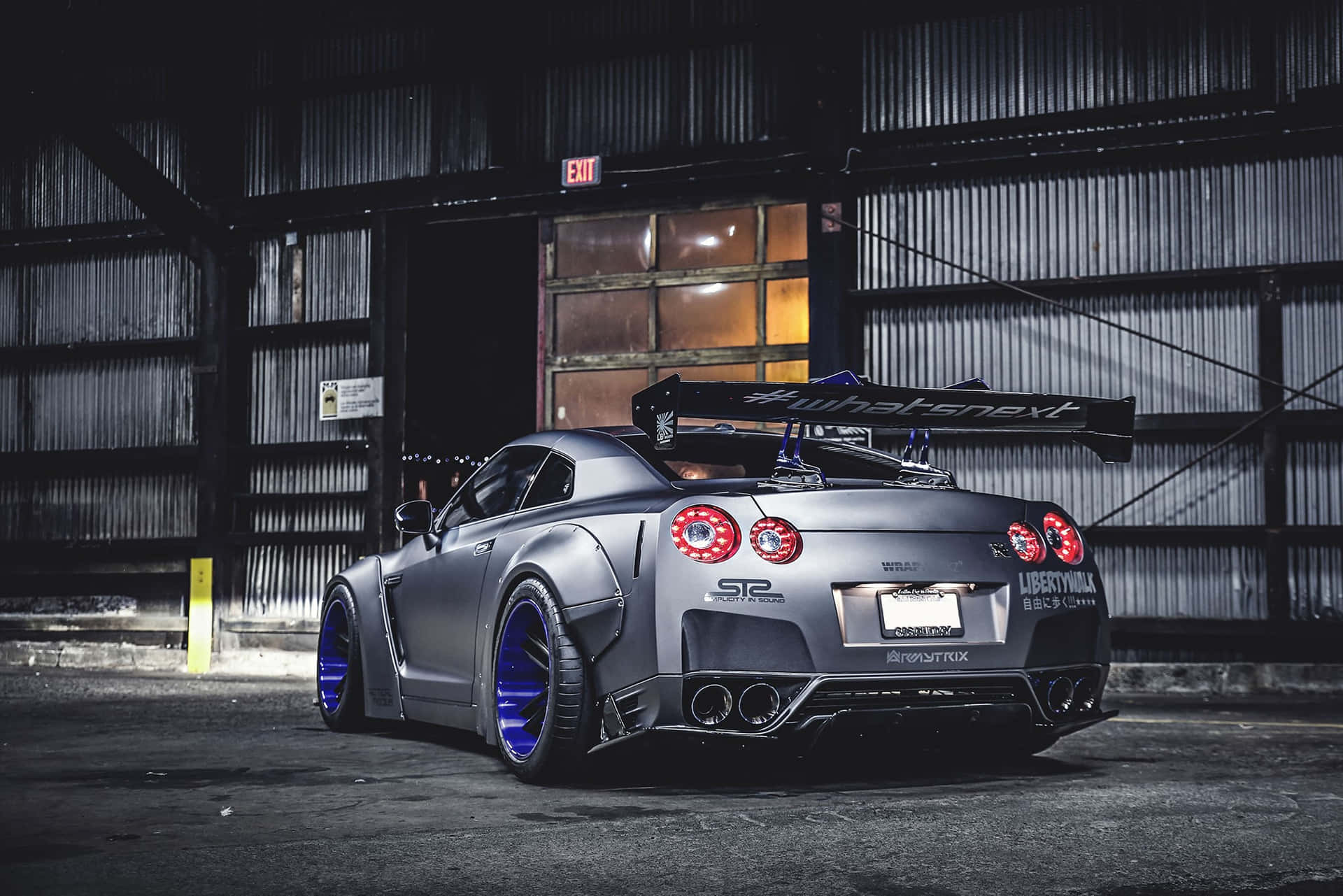 訂製啞光灰色日產GT-R，配備藍色輪圈，停泊在黑暗的倉庫中。