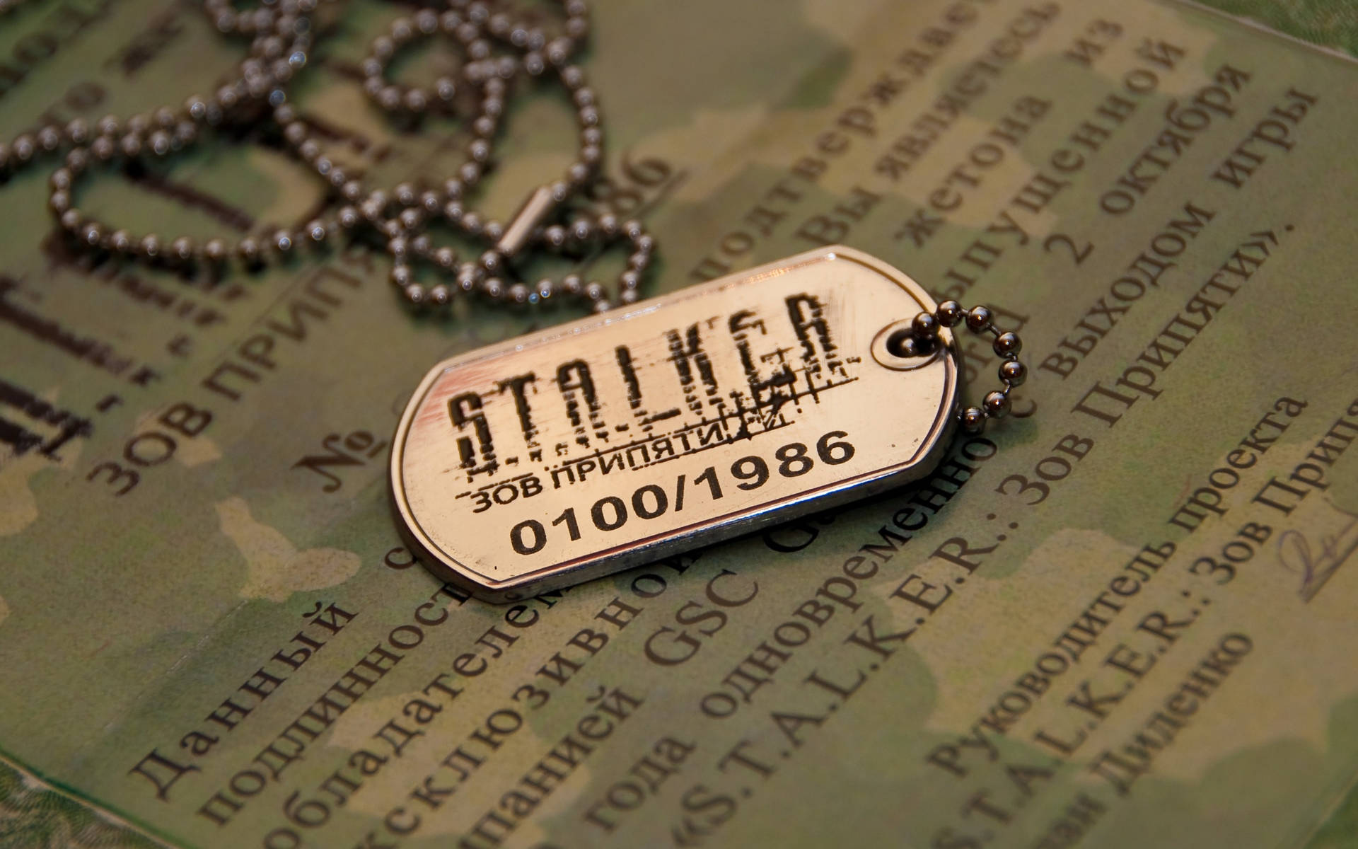 金屬狗牌，上面有「STALKER」和日期，放在帶有俄語文字的迷彩紙上。