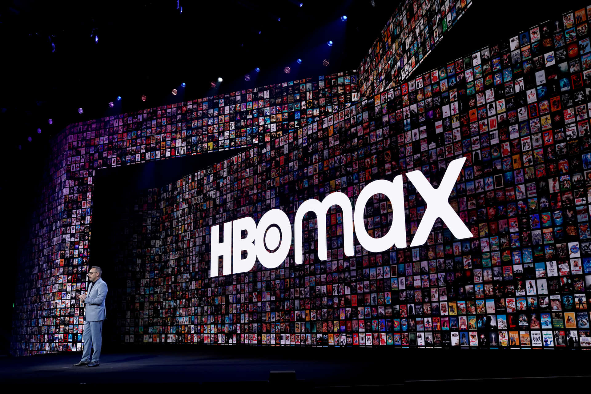 講者在HBO Max活動中進行演示，身後是一面電影海報牆。