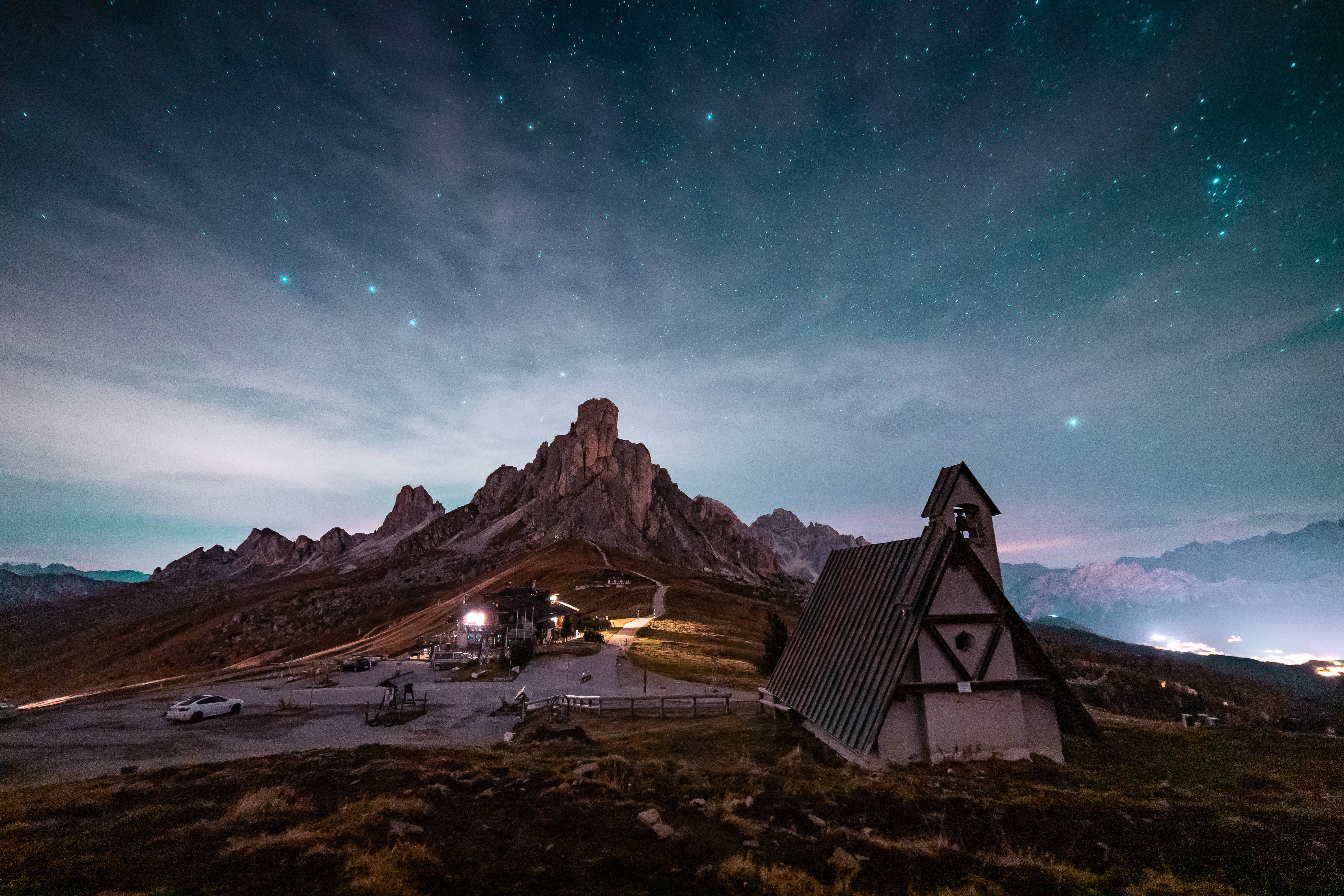 屋舍與山巔上方的夜空美學壁紙 壁紙 — 星空夜空照亮崎嶇的山峰和高山高原上孤獨的小教堂。