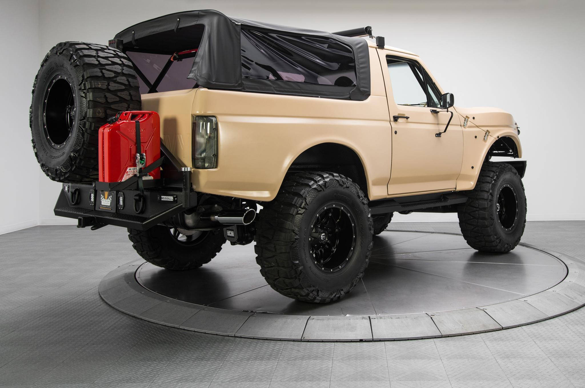 展廳內的福特 Bronco 壁紙 — 一輛米色升高版福特Bronco，配備黑色輪胎和安裝在黑色後保險槓上的紅色燃油罐，停在工作室的旋轉平台上。