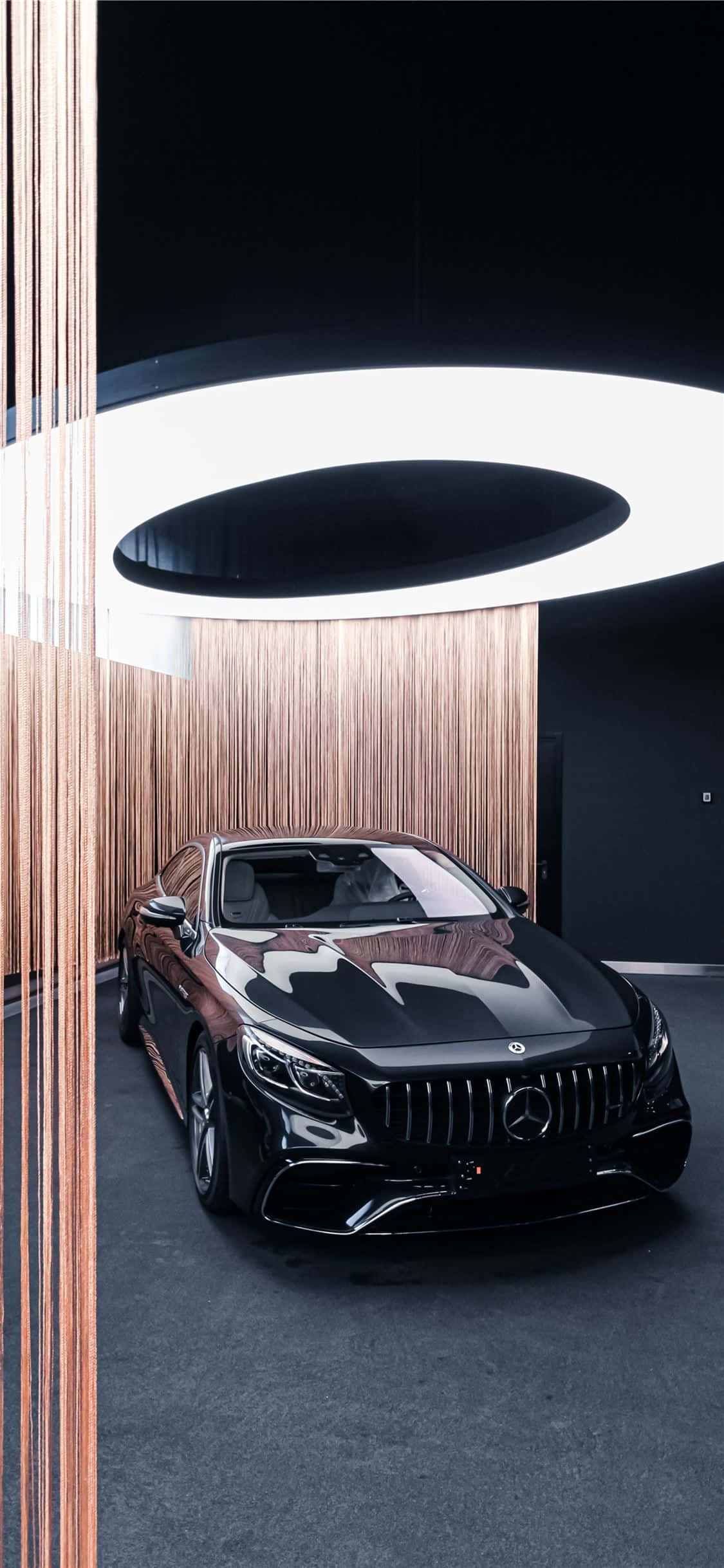 展廳黑色 iPhone Xs Mercedes AMG 背景 壁紙 — 一輛時尚的黑色平治S-Class房車在現代木牆展廳中，在發光的圓形天花燈下閃閃發光。