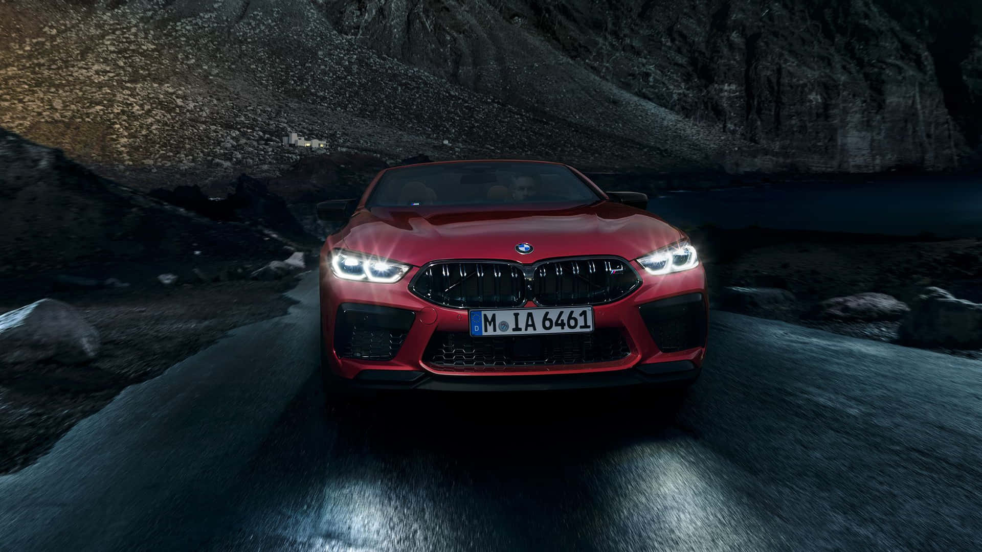 紅色BMW M8 Coupe在夜間穿過湖邊的山區地形。