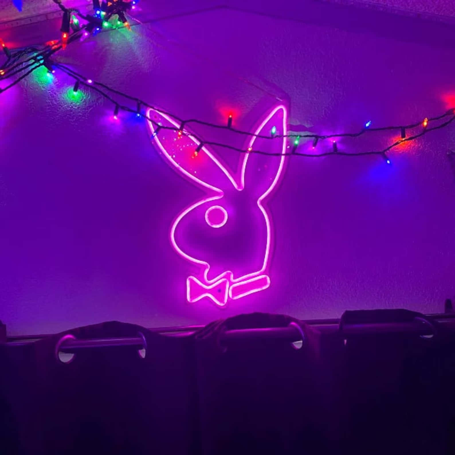 粉紅色霓虹燈 Playboy 兔子標誌，帶有彩色燈串，位於紫色牆上。