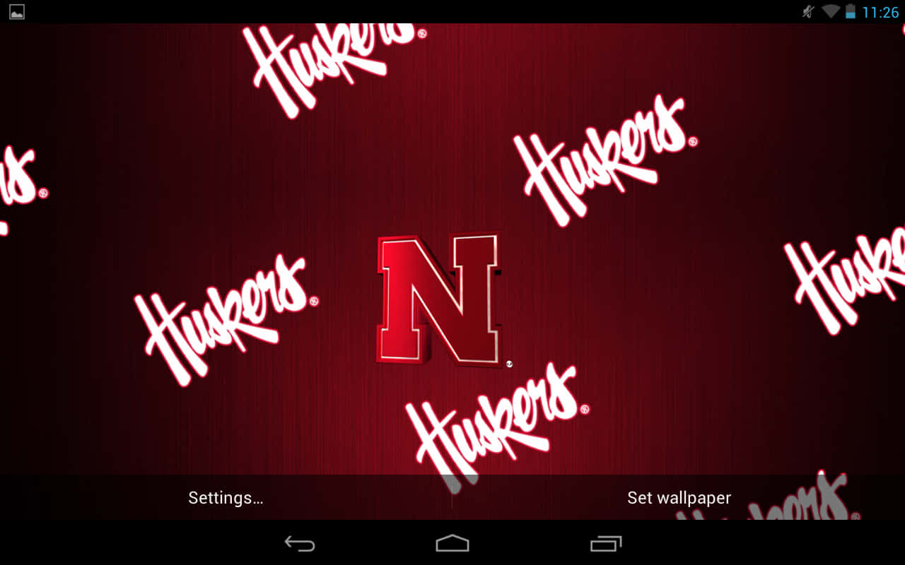 展現你的紅魔精神，高舉隊旗！ 壁紙 — 一張大膽的紅色壁紙，中央有 Huskers 'N' 標誌，周圍散落著白色草書 Huskers 文字，背景為有紋理的深紅色。