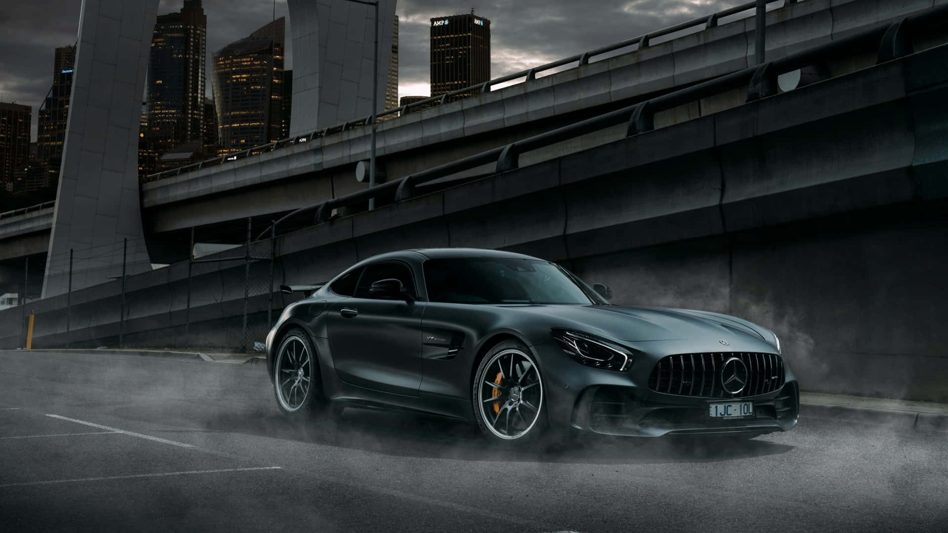 黑色 Mercedes-AMG GT 在黃昏時分在高架橋下的潮濕街道上飄移。