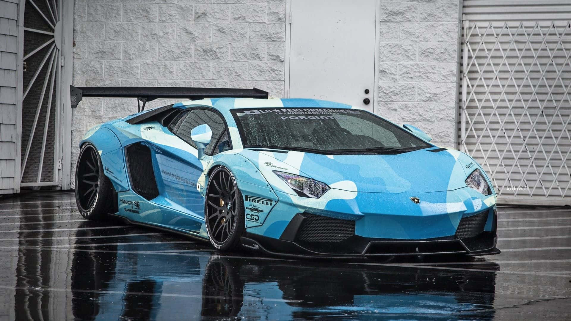 淺藍色林寶堅尼 Aventador 帶有賽車塗裝，停在車庫附近的濕瀝青路面上。