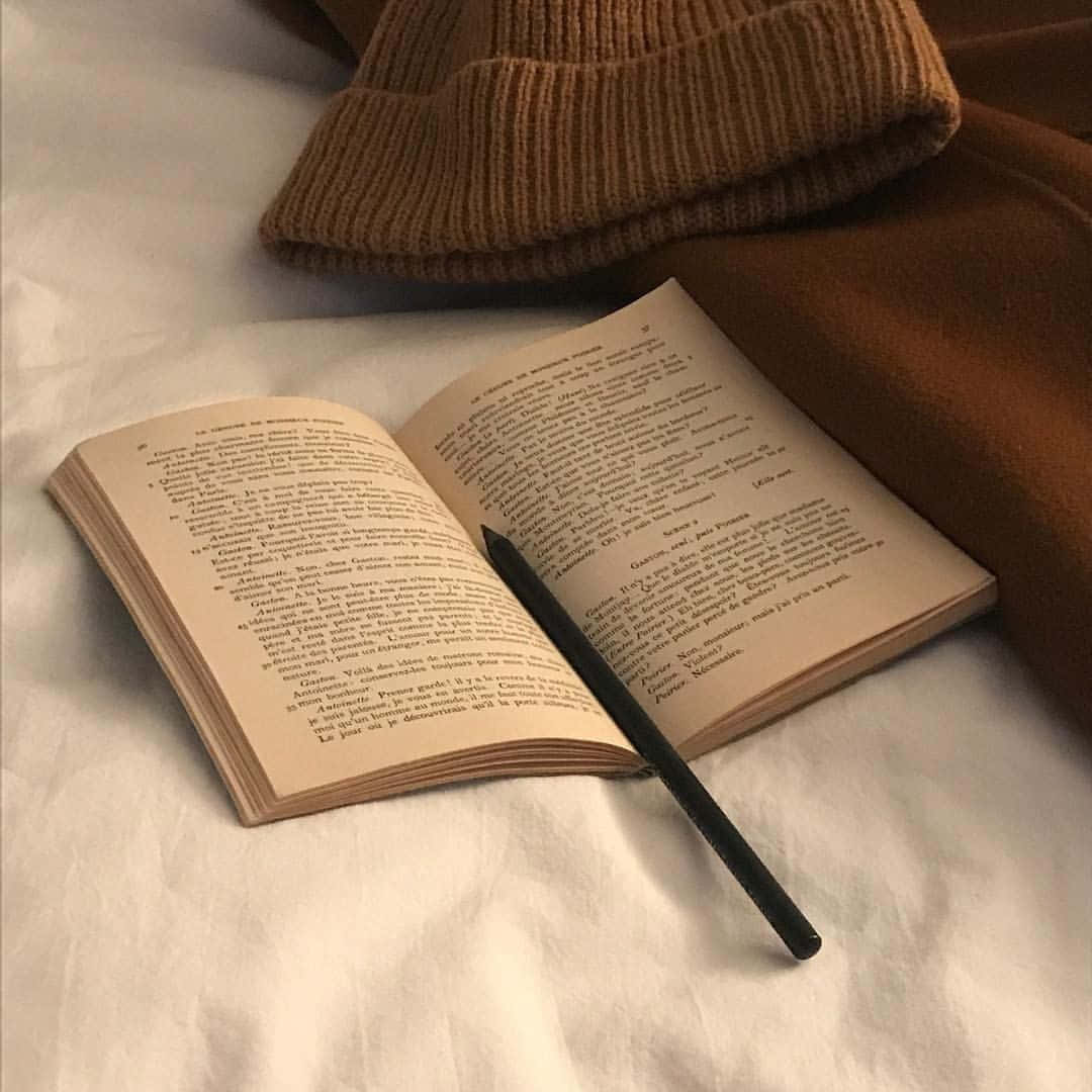 打開的書，附有筆和針織帽，放在床上供閱讀。