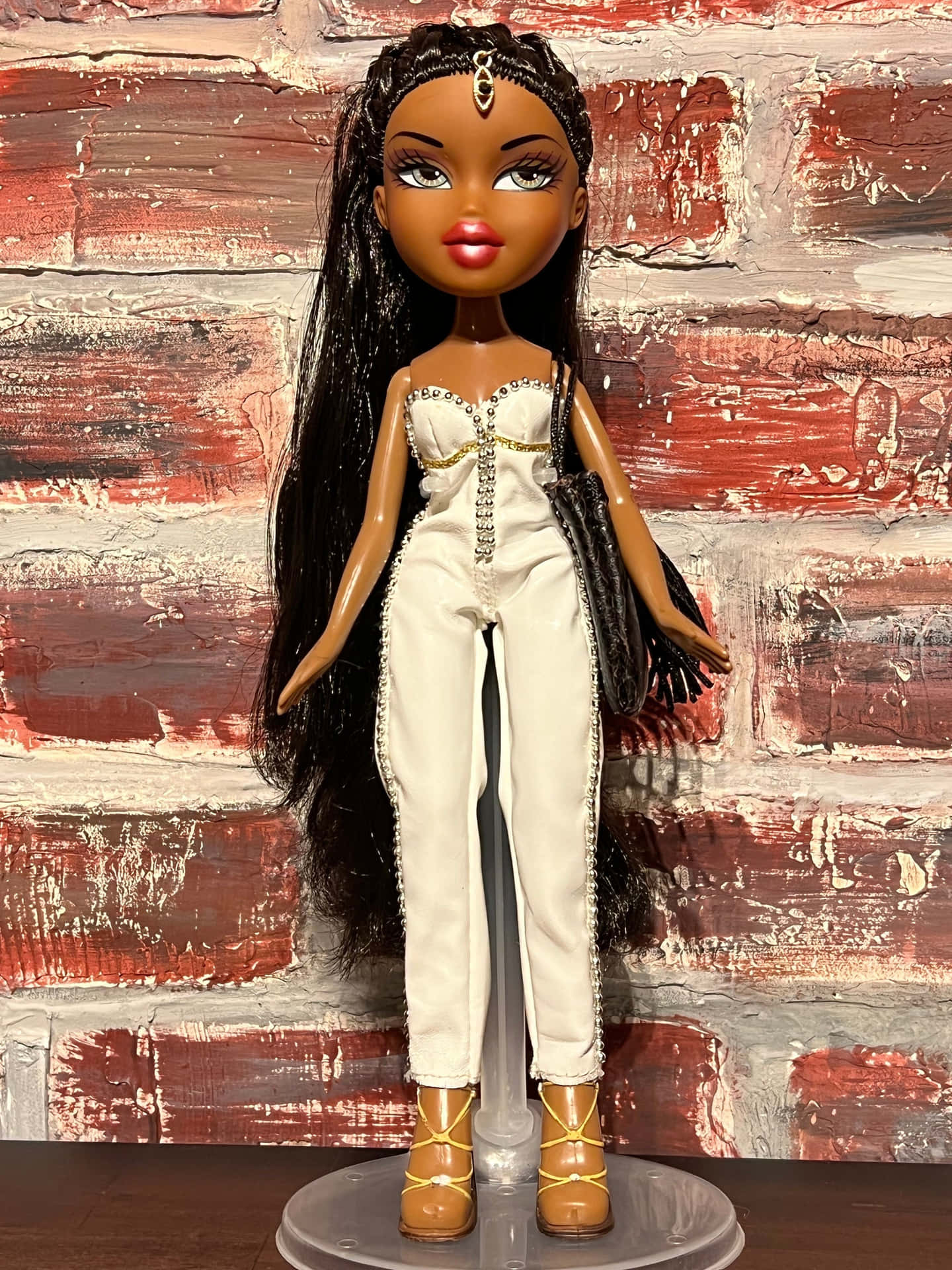 Bratz 公仔穿著白色連身褲和棕色靴子，背景為紅磚牆。
