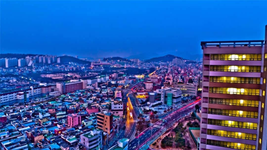黃昏時分的城市天際線，燈火通明的建築物和移動的交通燈光。