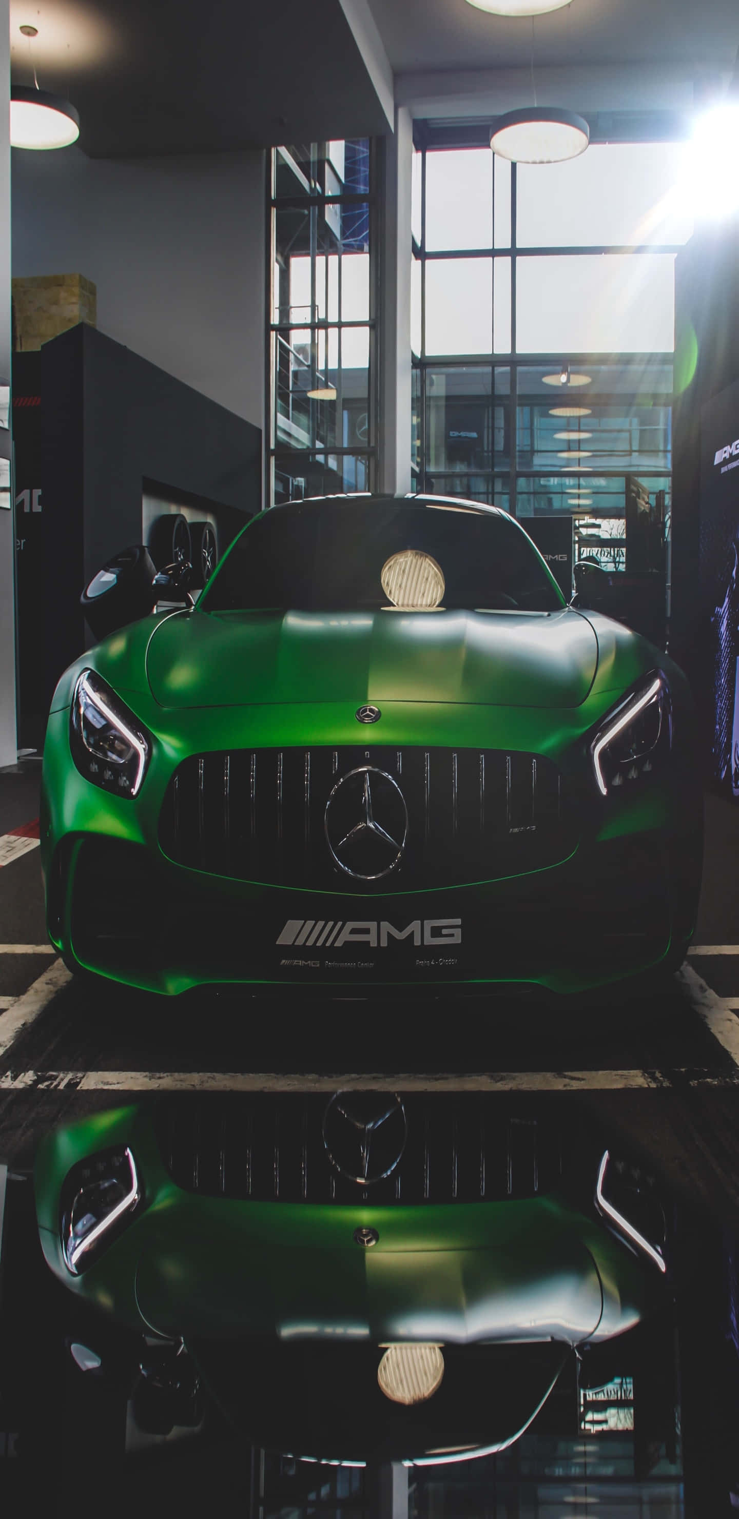 展示廳內的綠色梅賽德斯-奔馳 Pixel 3XL AMG GT-R背景 壁紙 — 一輛光亮的綠色Mercedes-AMG跑車在現代化展廳的明亮燈光下閃耀，地板反射出車身光澤。
