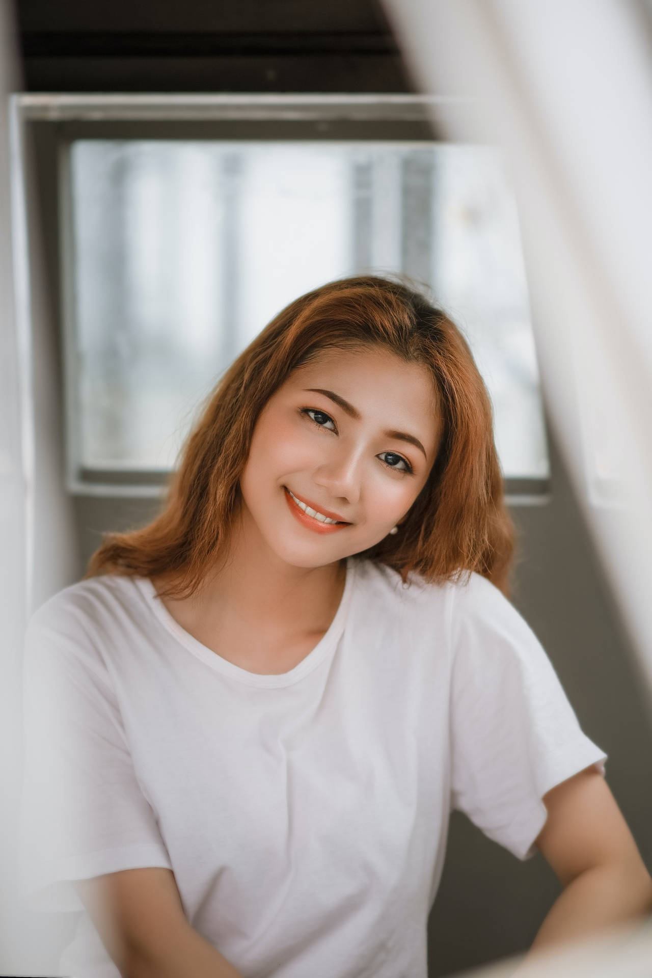 年輕女性在窗邊穿著白色T恤微笑