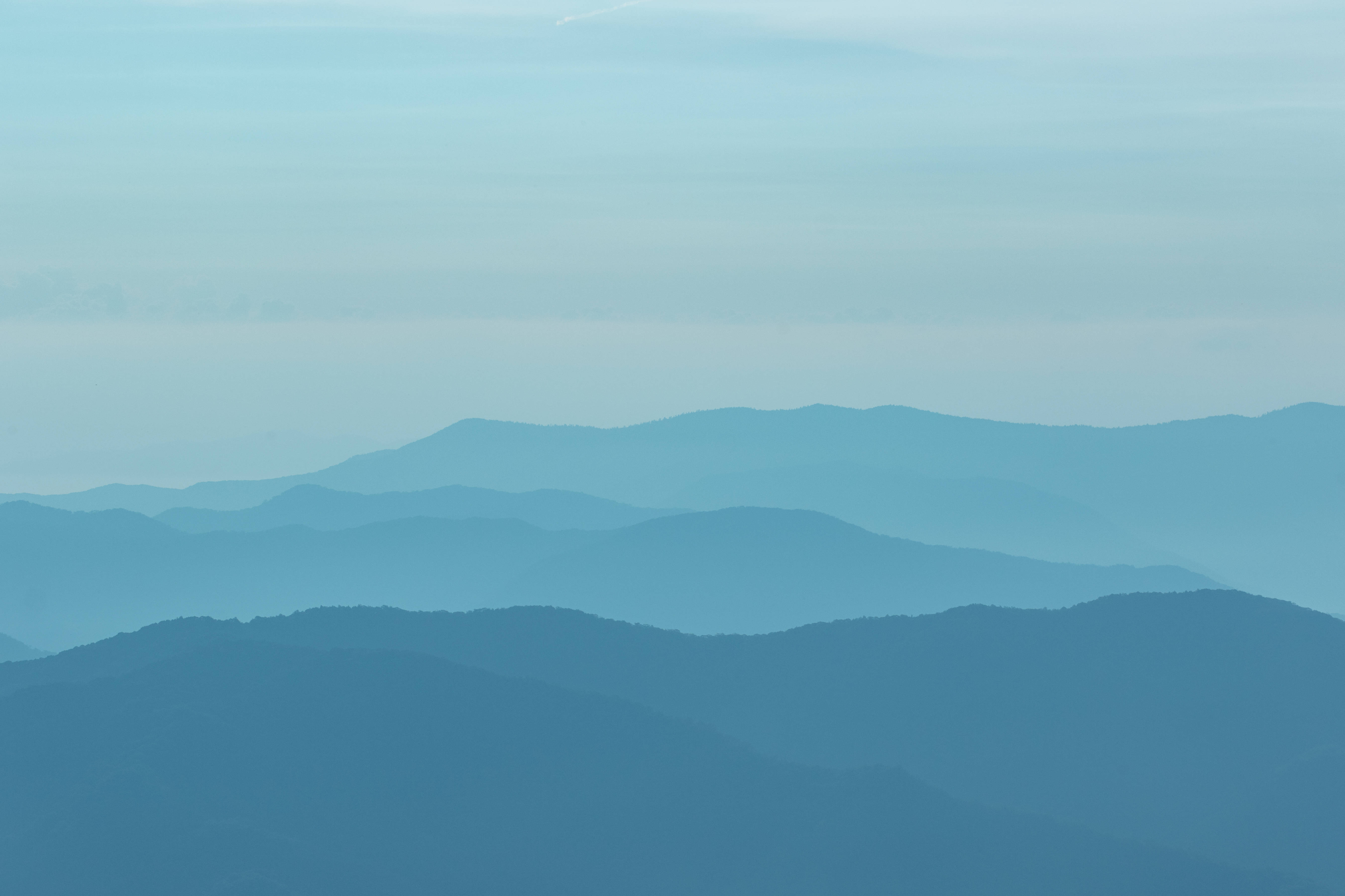 Ombre Blue Teal Mountain 壁紙 — 層層疊疊的山脈在柔和天空下逐漸融入迷濛的藍色霧靄中。