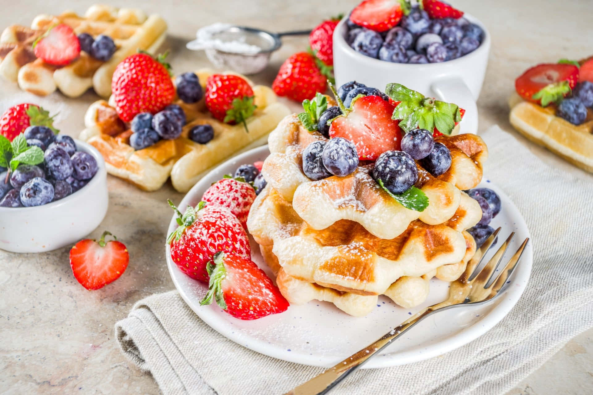 Waffle 桌布 壁紙 — 層層疊起的金黃色窩夫，上面鋪上新鮮草莓、藍莓和薄荷葉，撒上糖粉。