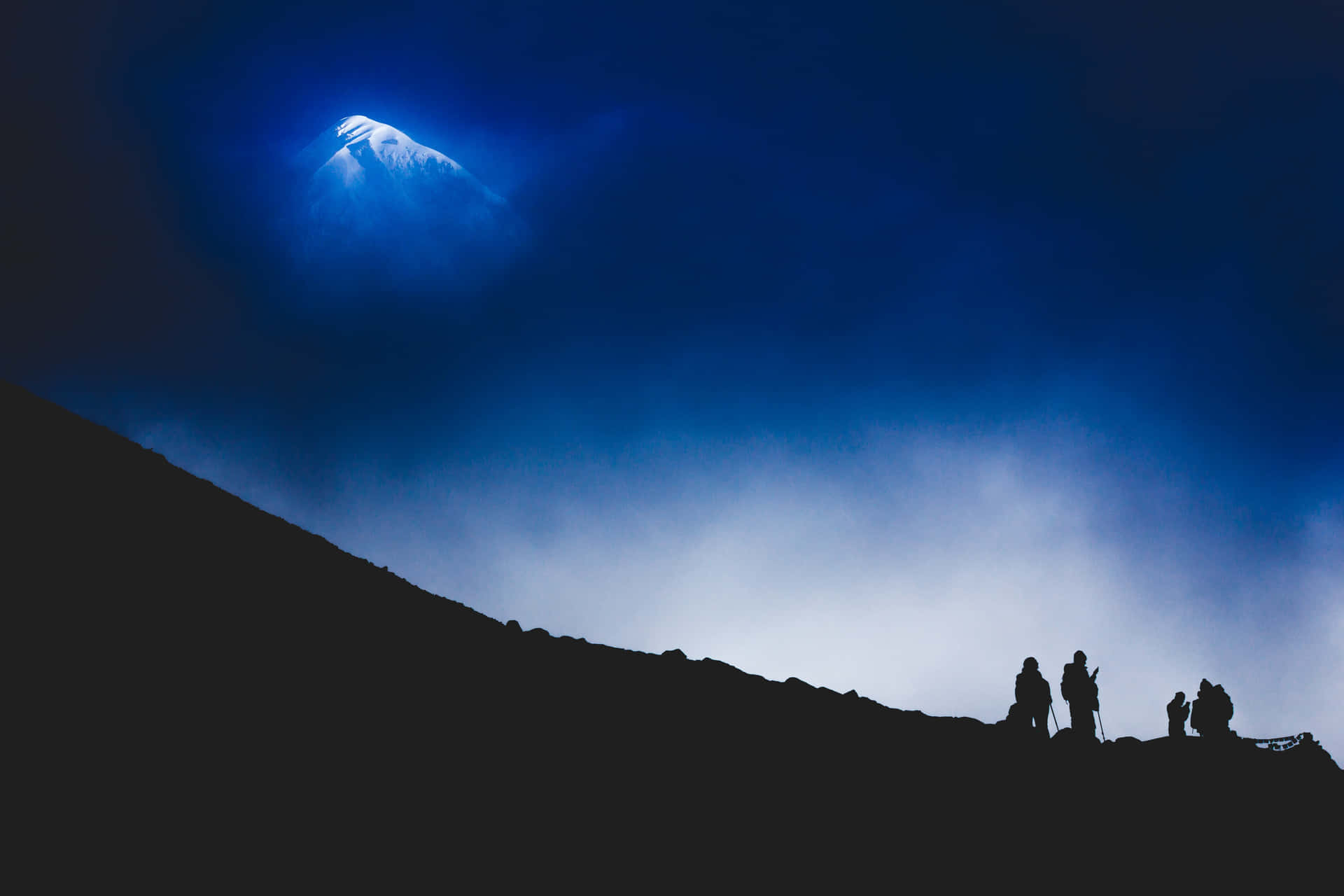 夜晚發光藍色山峰映襯下的登山者剪影。