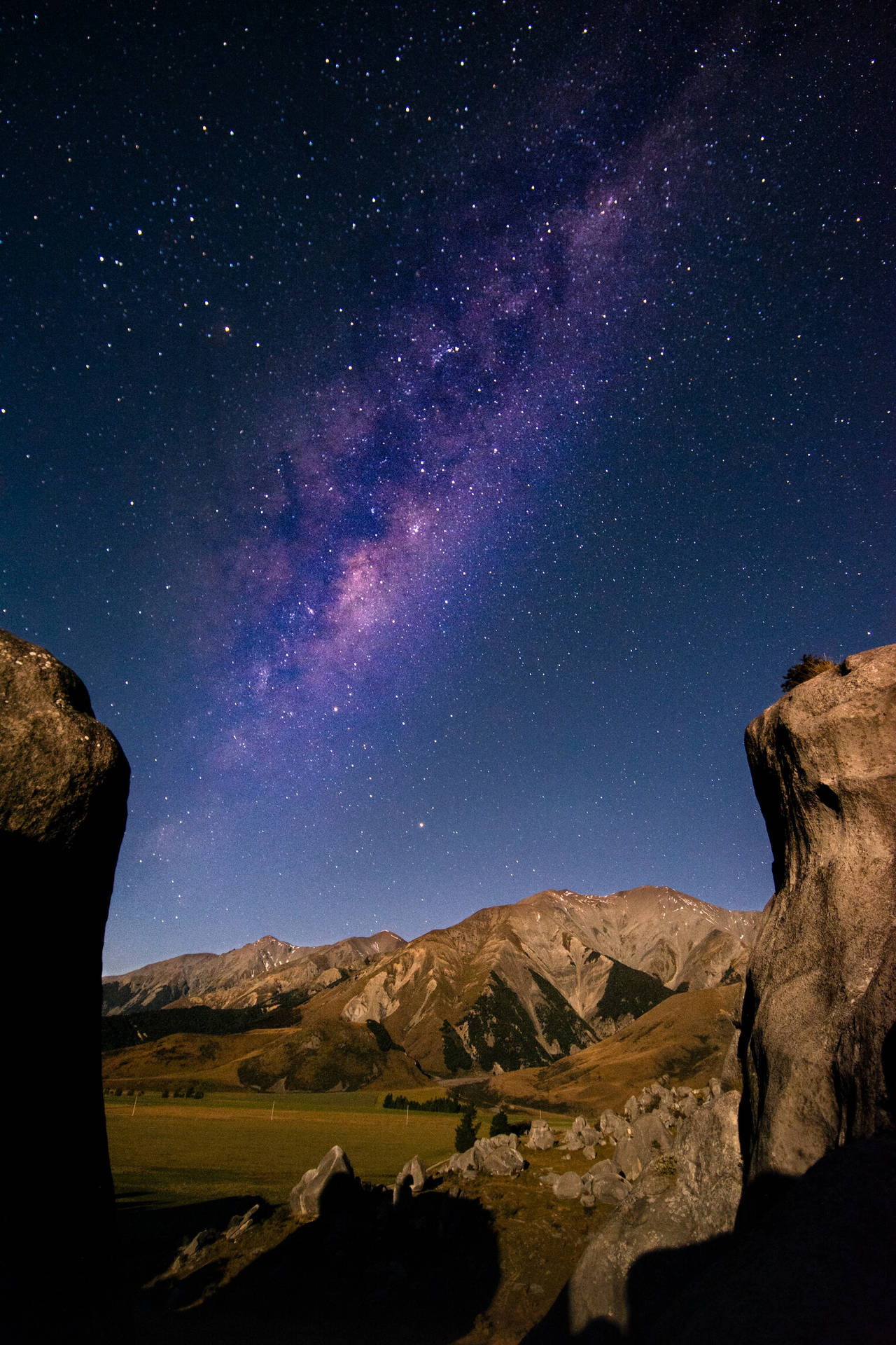 銀河系在夜間山脈上方發光，由岩石框住