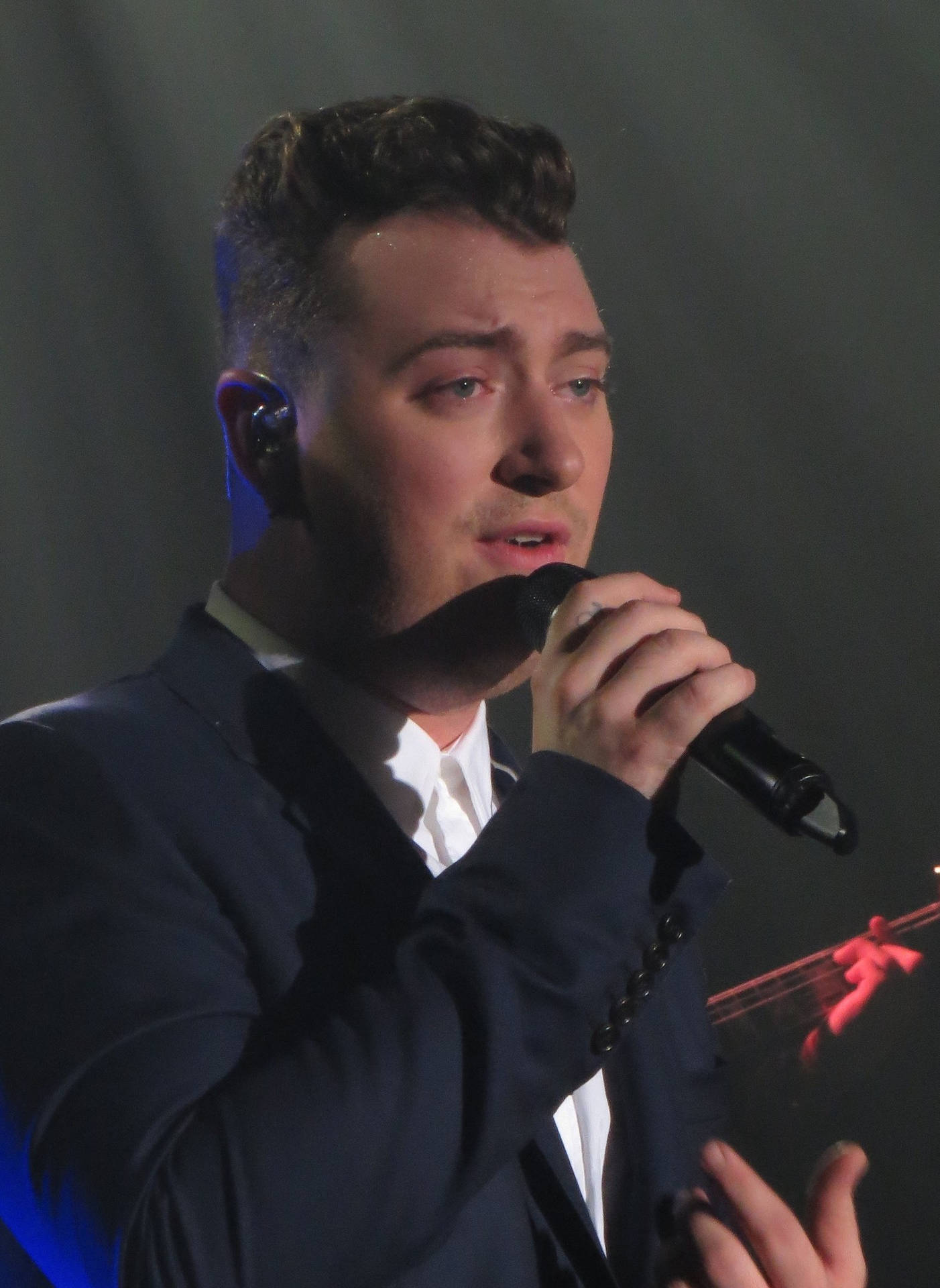 Sam Smith 在燈光璀璨的舞台上對著麥克風唱歌。