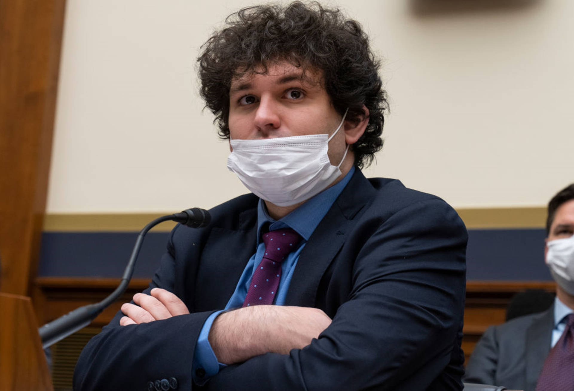 身穿西裝及口罩的男子在法庭內交叉雙臂坐著