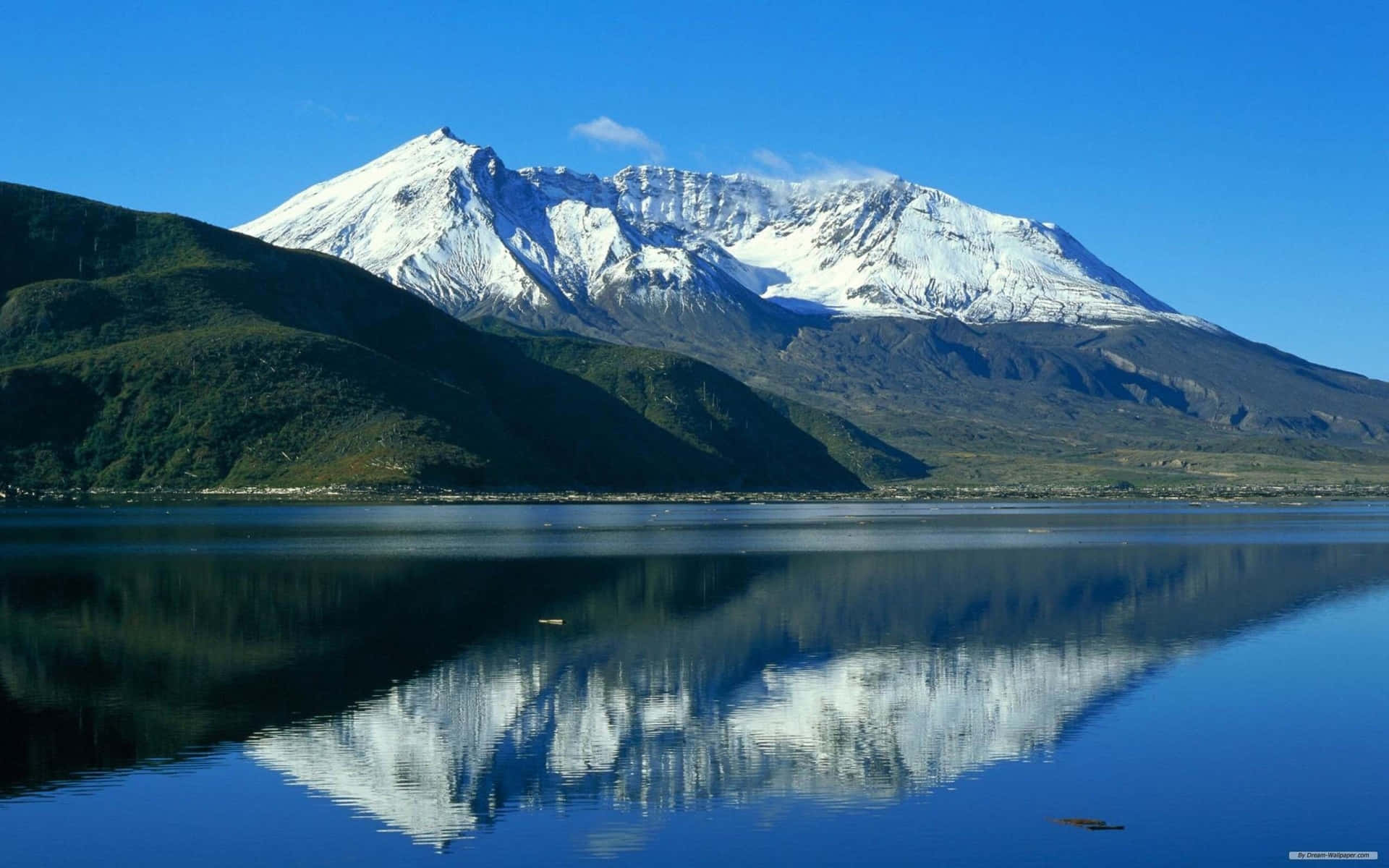 積雪的山峰完美地倒映在寧靜的藍色湖面上，天空明亮。