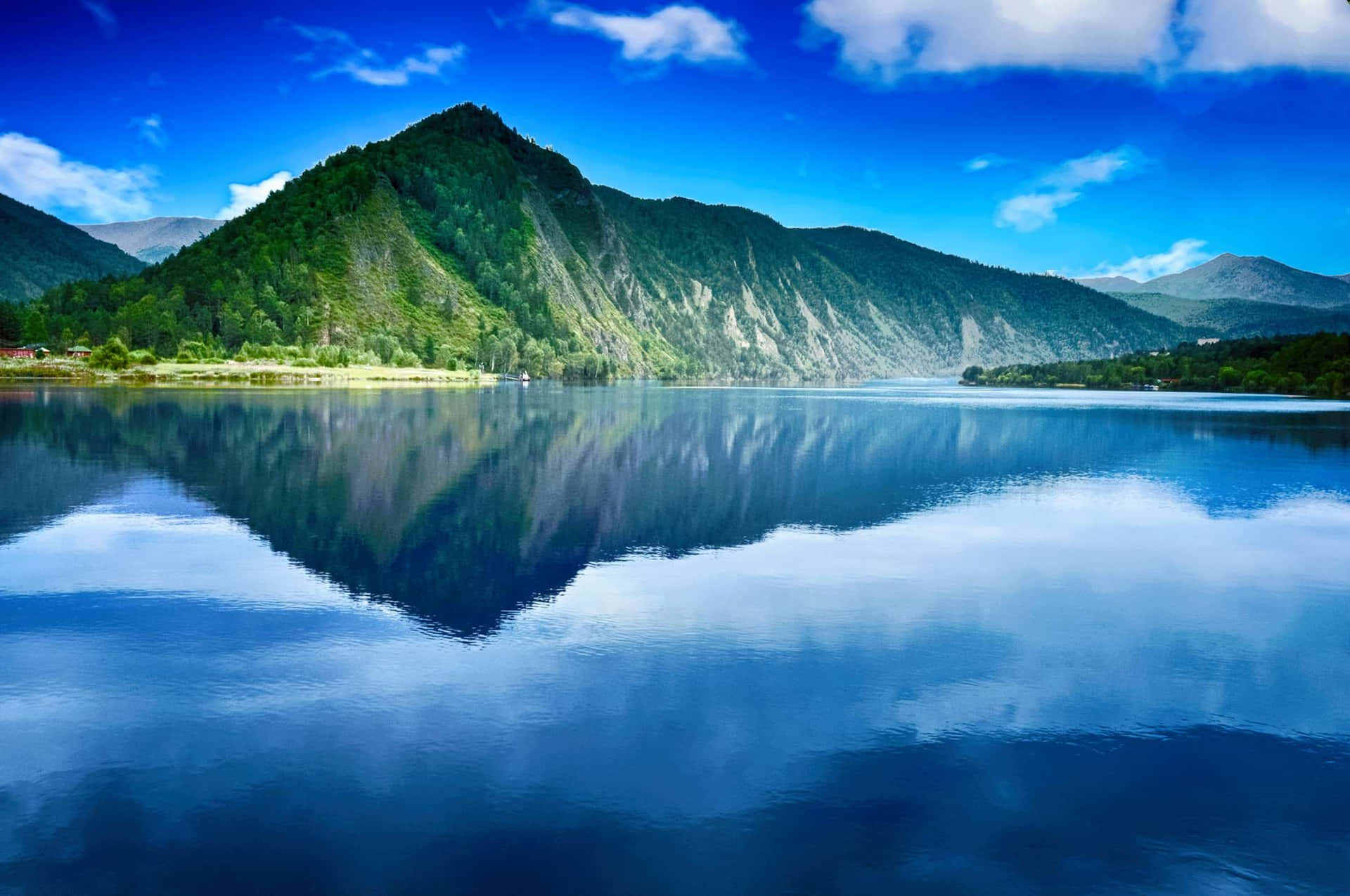 晴朗日子裡平靜的山間湖泊映照著藍天和綠丘。