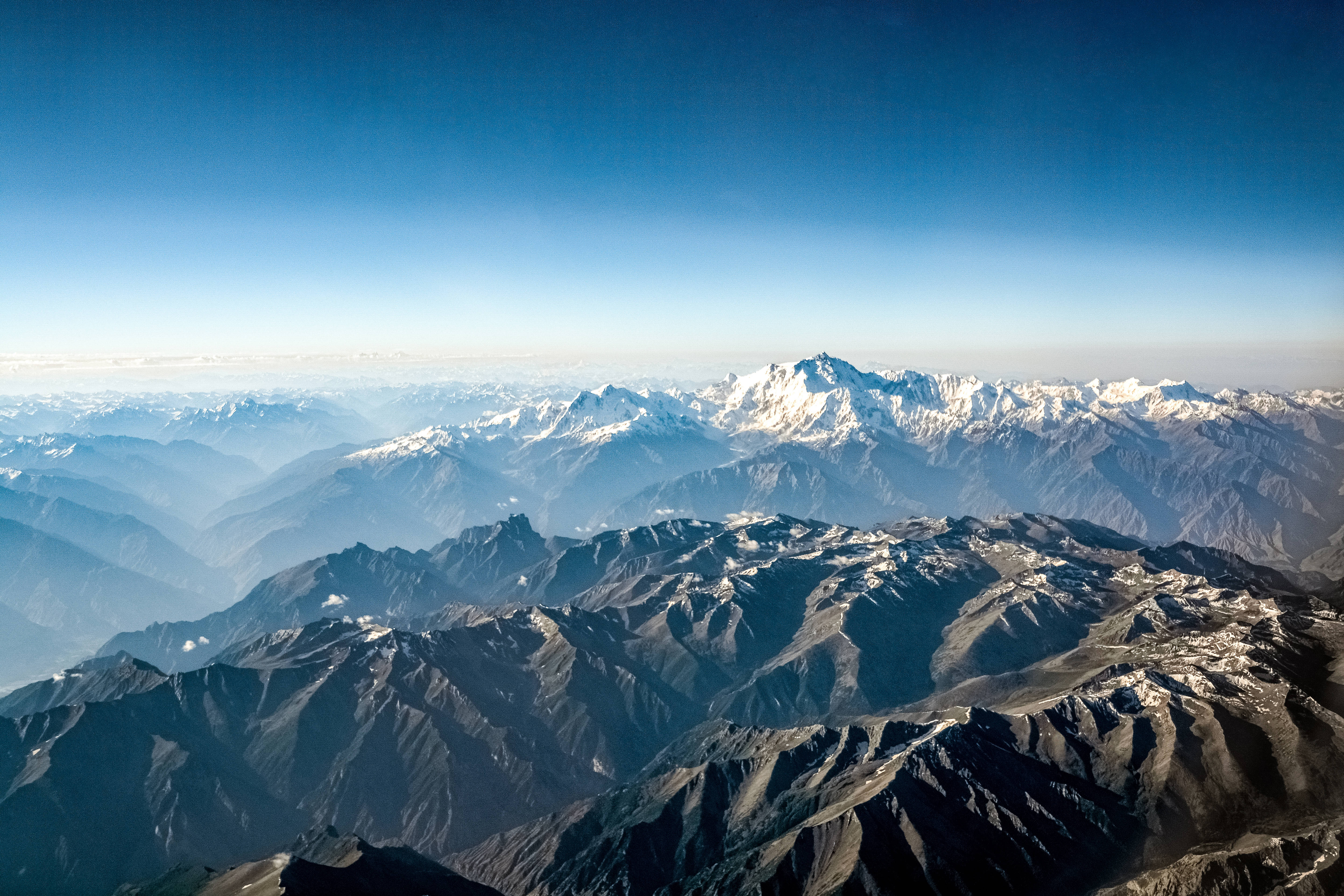 山嶺空中地貌 壁紙 — 令人嘆為觀止的鳥瞰圖，展現層層疊疊的山脈，白雪覆蓋的山峰在清澈的藍天下。