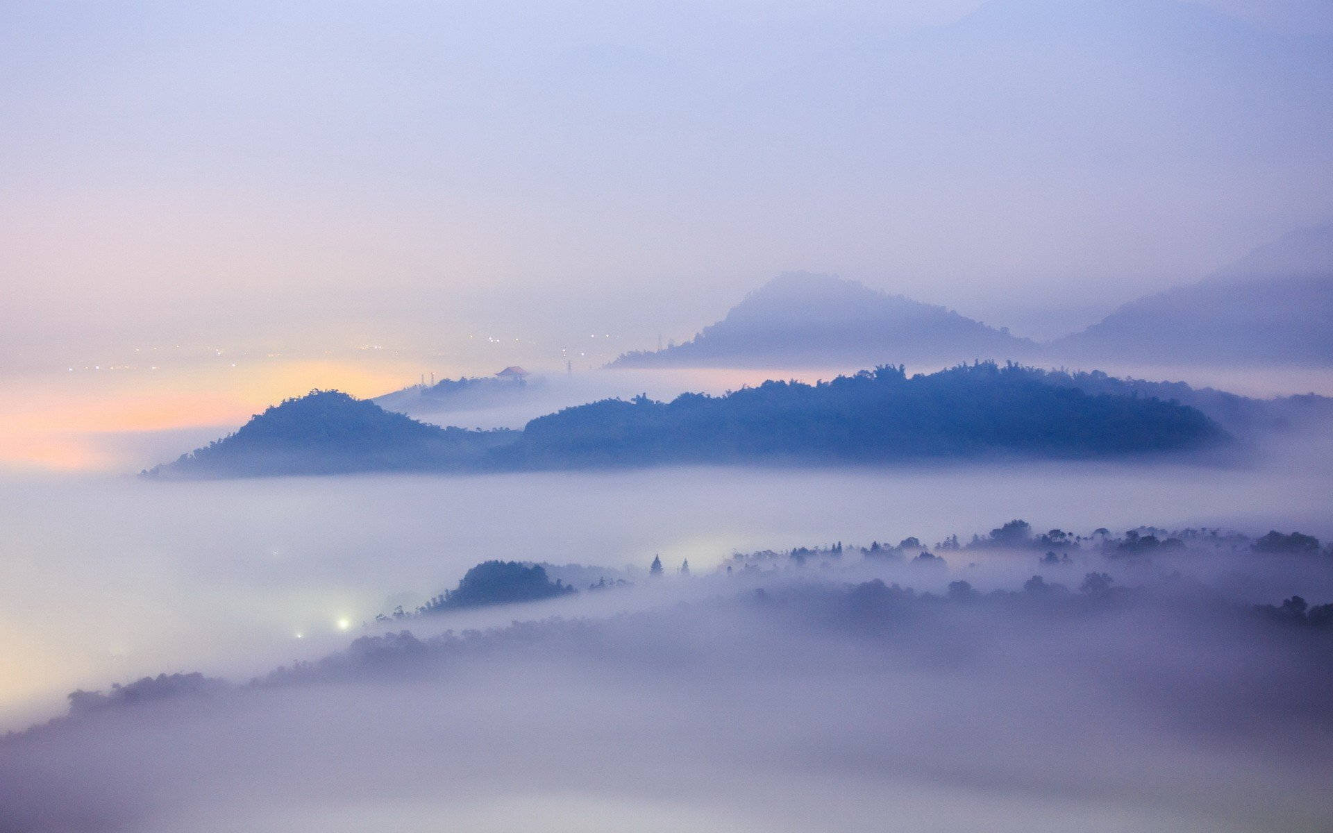 黎明時分從霧中浮現的山巒，天空呈現柔和的紫色和橙色。
