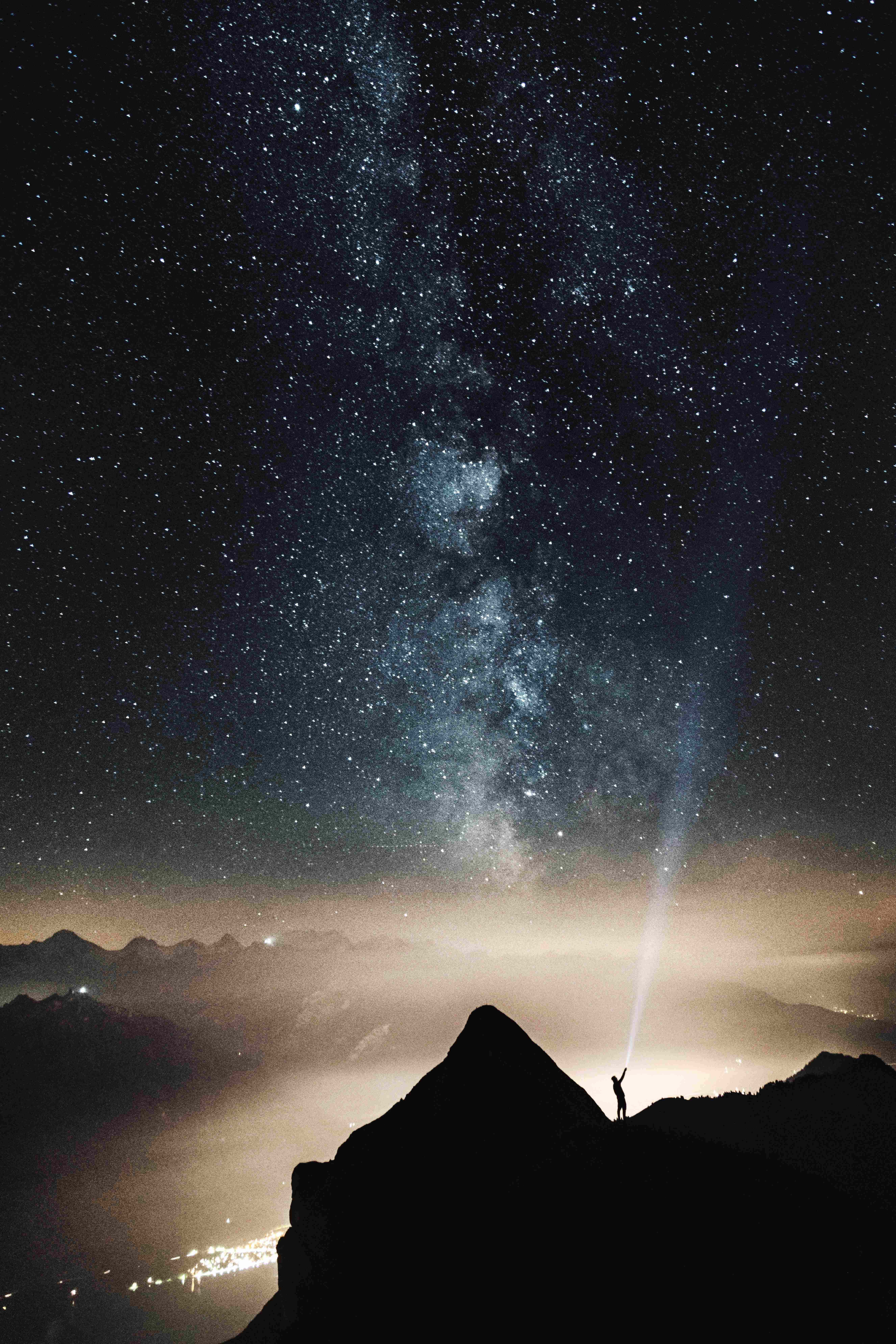 山巔男子剪影 iPhone 背景 壁紙 — 一個孤獨的身影夜晚站在山頂，將手電筒向上照向銀河系。