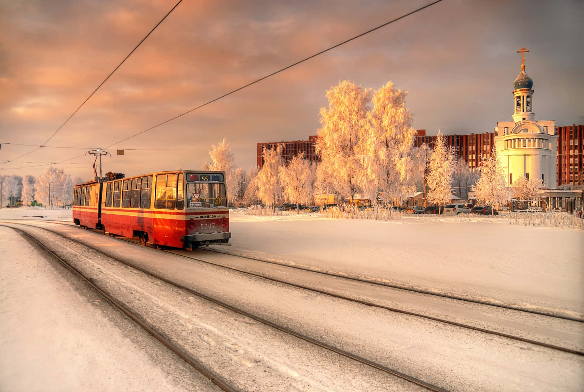 日落時分，紅色電車在結霜樹木和教堂附近的雪地軌道上行駛。