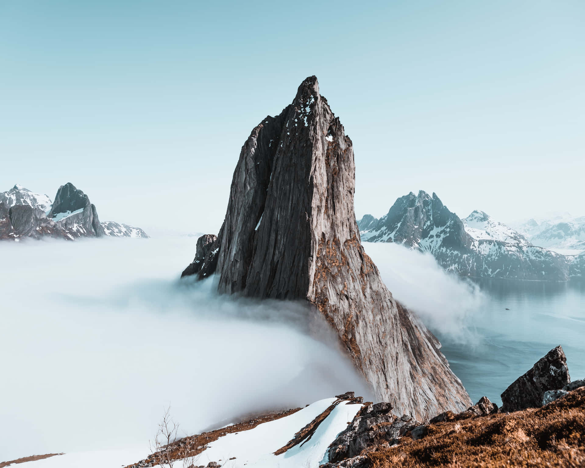 一座鋸齒狀的山峰從雲層中浮現，下方是白雪覆蓋的山峰和寧靜的水面。