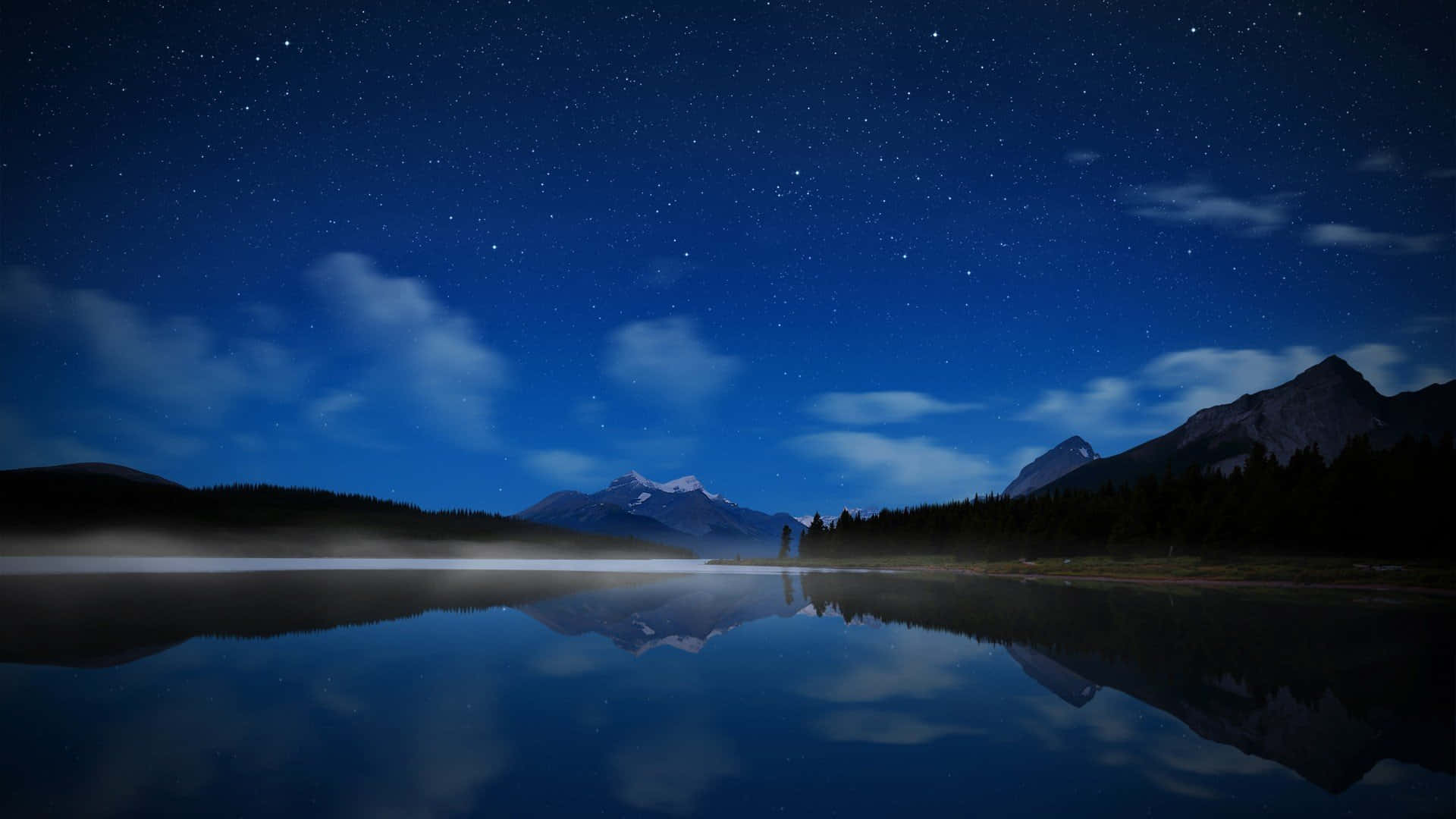 山湖夜空 壁紙 — 繁星點點的夜空完美地倒映在平靜的湖面上，四周環繞著黑暗的山脈和森林。