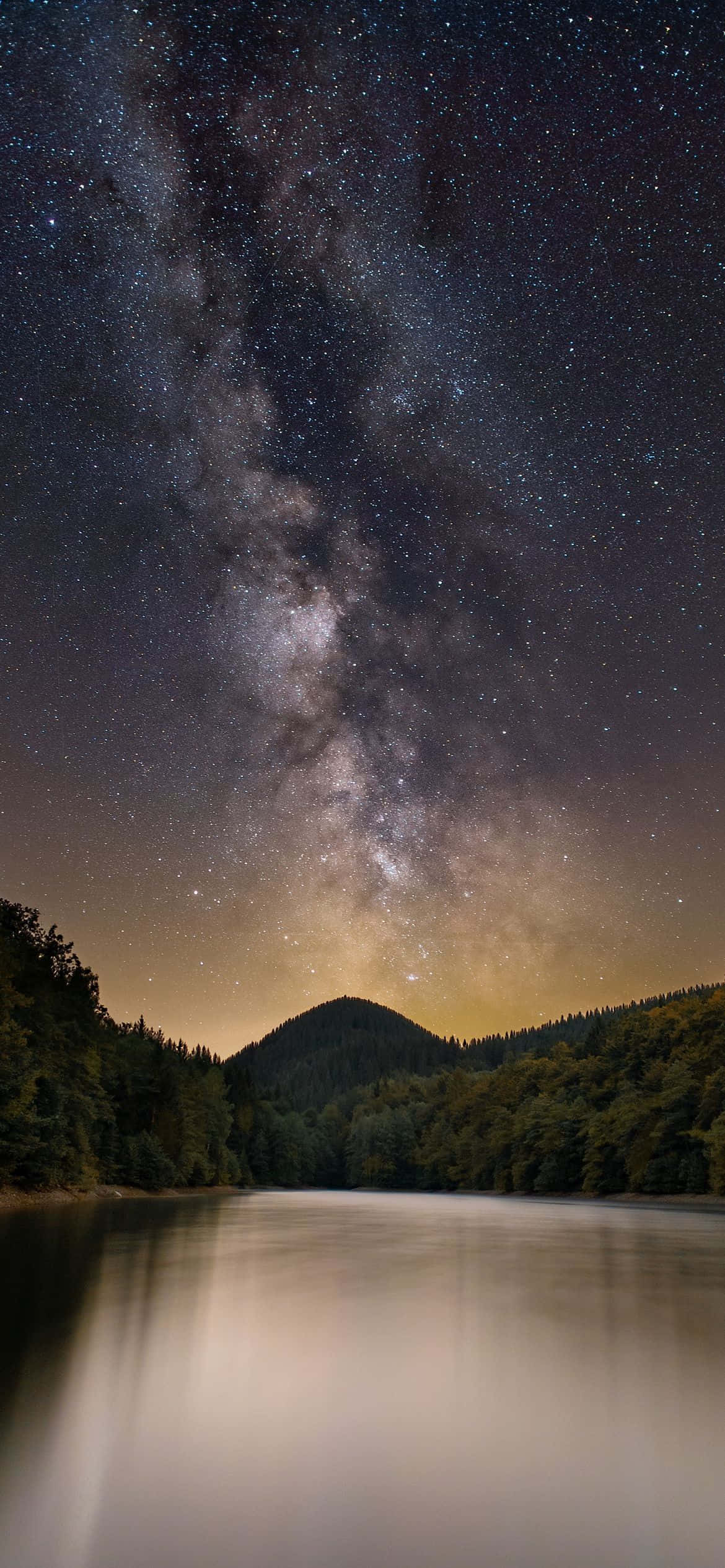 山脈後方的日出 壁紙 — 銀河系在深邃夜空下，於寧靜的湖面上方彎曲，湖面映照著星星和森林覆蓋的山丘。