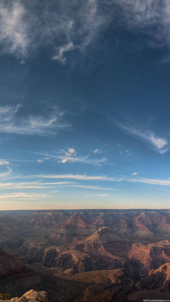 山脈自然 iPhone 背景 壁紙 — 廣闊的峽谷在戲劇性的天空下延伸，天空中有縷縷雲彩和深藍色調。
