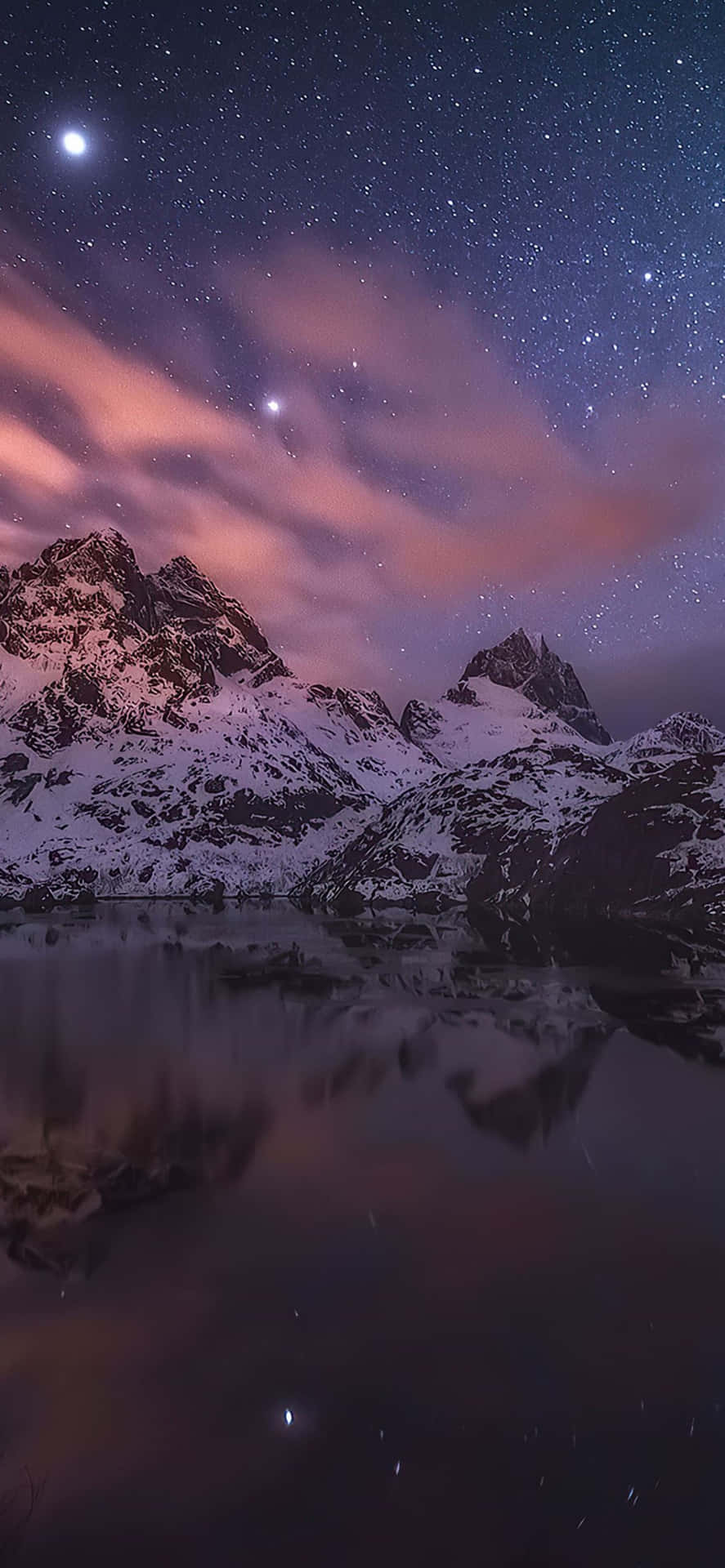 積雪的山峰在繁星點點的夜空下倒映於平靜的水面，伴隨著粉紅色的雲朵。