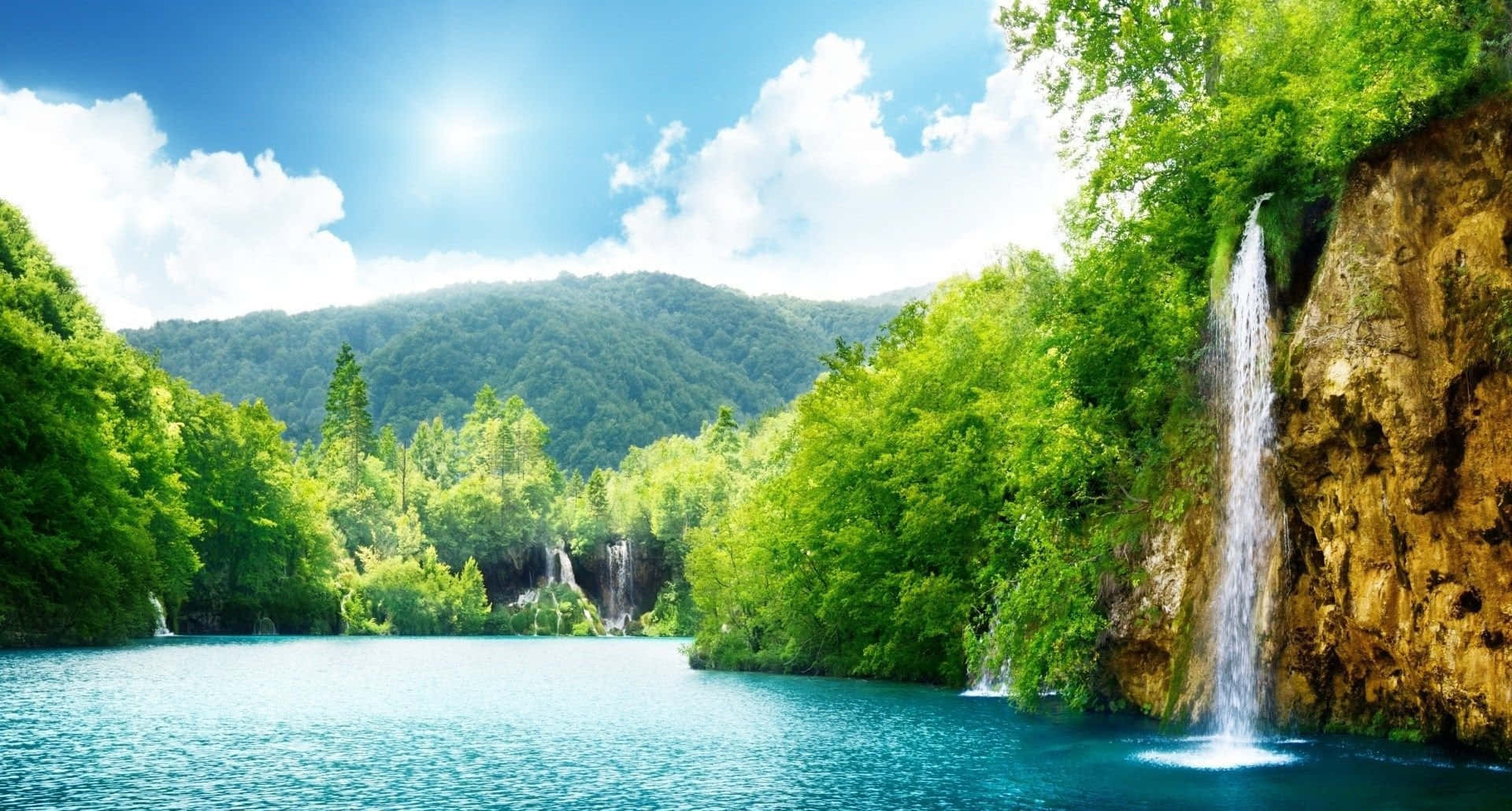 一個寧靜的湖泊，瀑布在陽光明媚的天空下流經森林覆蓋的山谷。