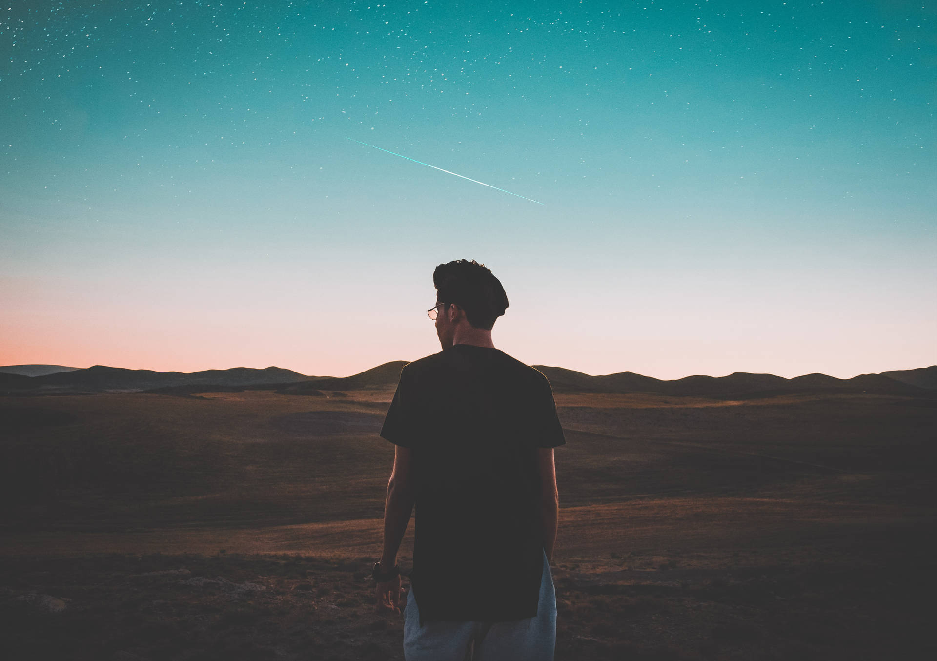 一個剪影中的男人站在沙漠中，觀看暮色天空中的流星。