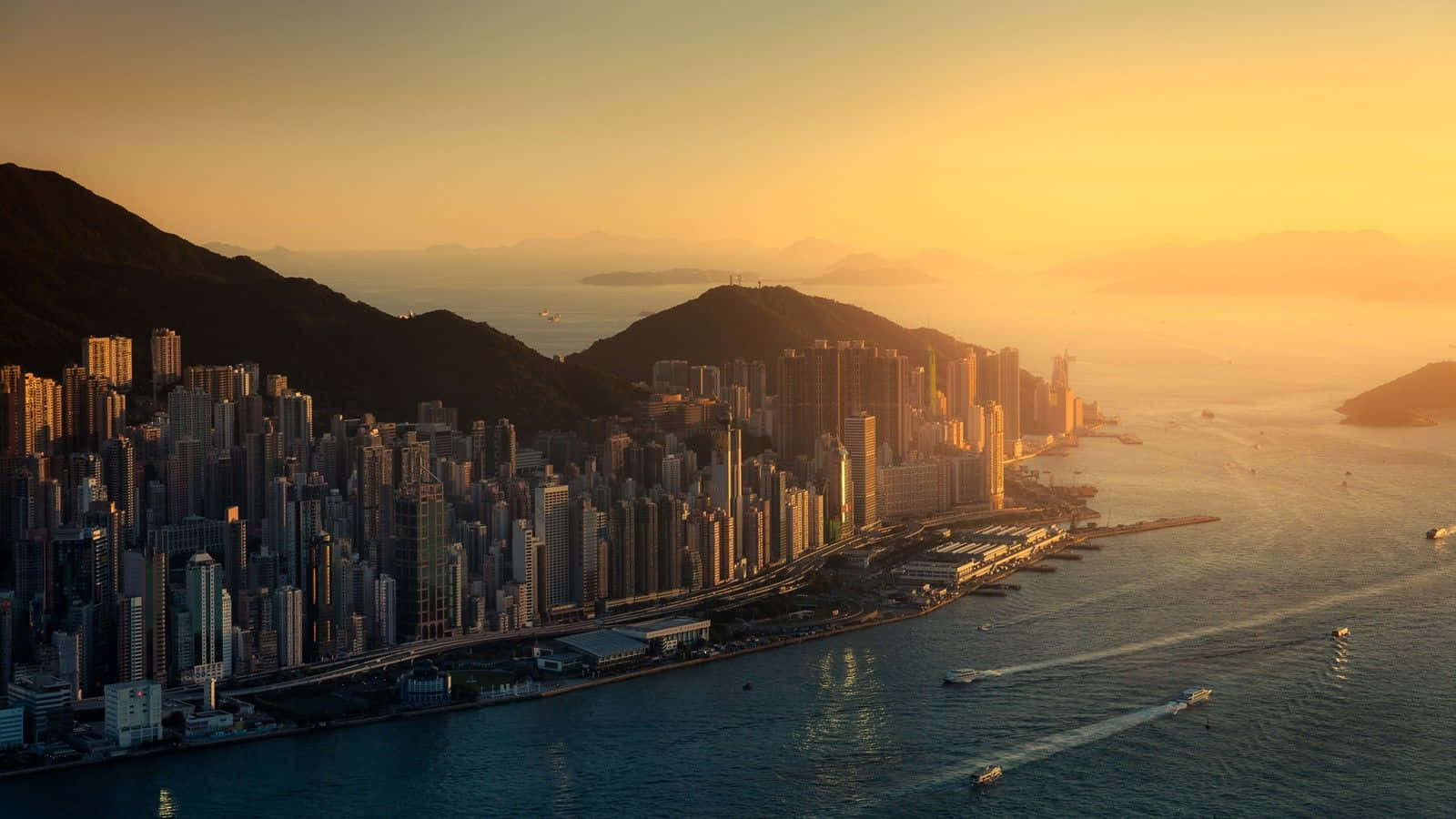 日落時的香港天際線，高樓大廈和水上的船隻。