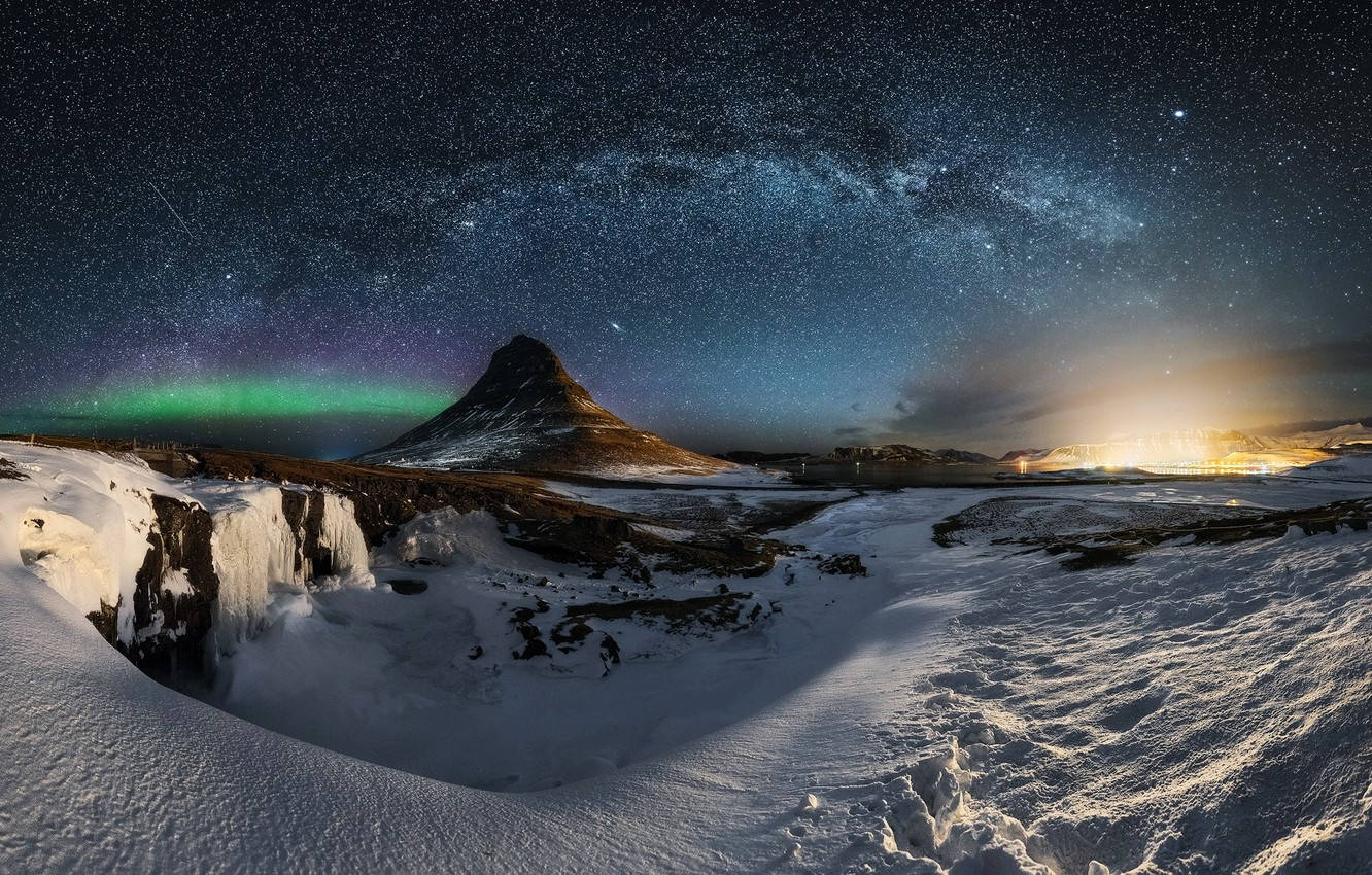 積雪的山峰，極光和星空下，夜晚燈火通明的城鎮。