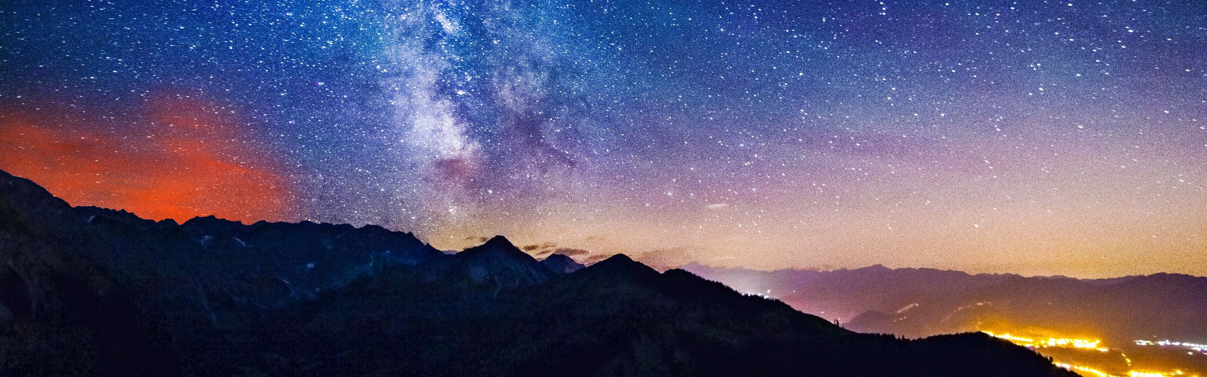 夜晚山脈上空的銀河系與閃爍的山谷燈光。