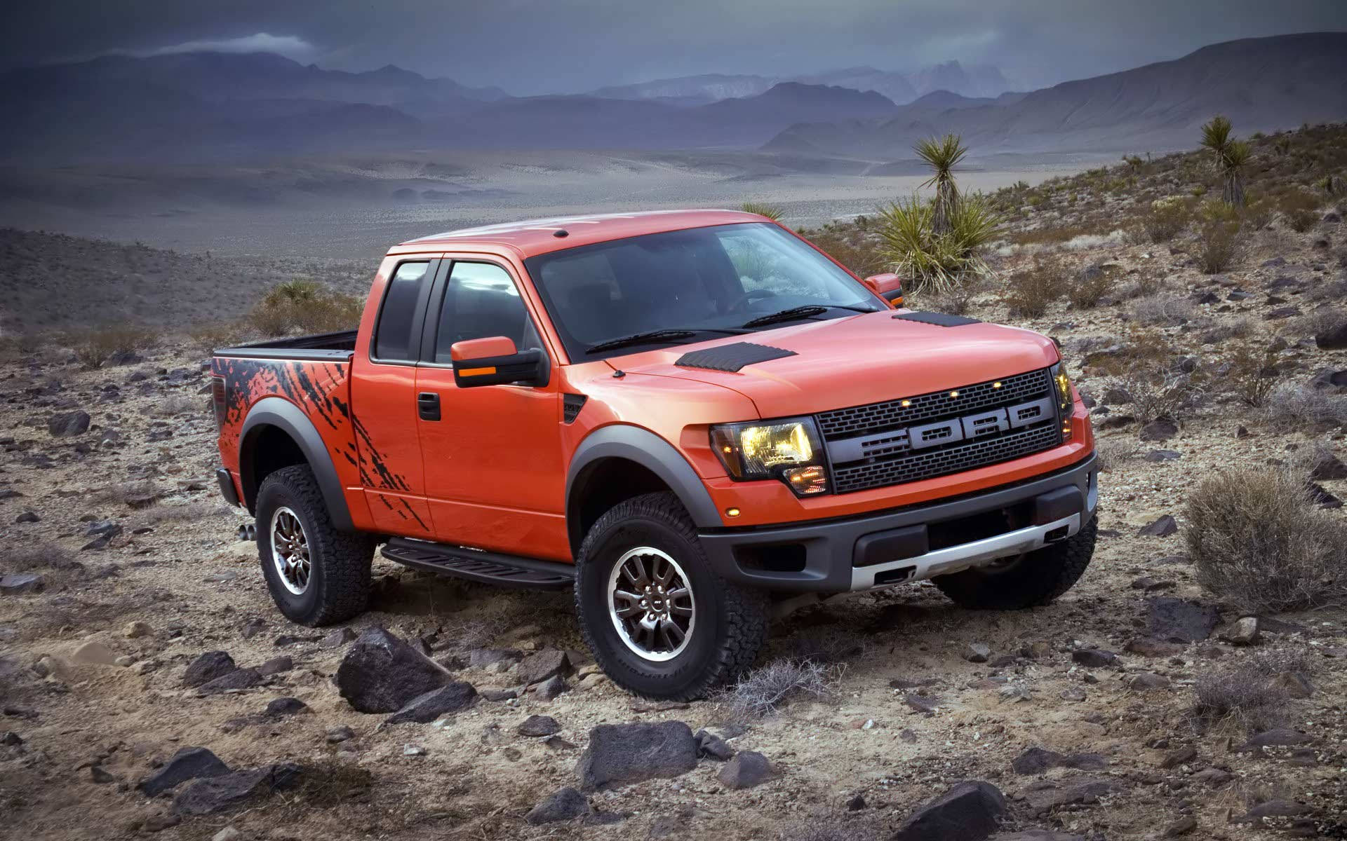 岩石地形酷炫卡車 壁紙 — 一架大膽的橙色Ford F-150 Raptor在陰沉多雲的天空下，堅固地矗立在岩石沙漠地形上。