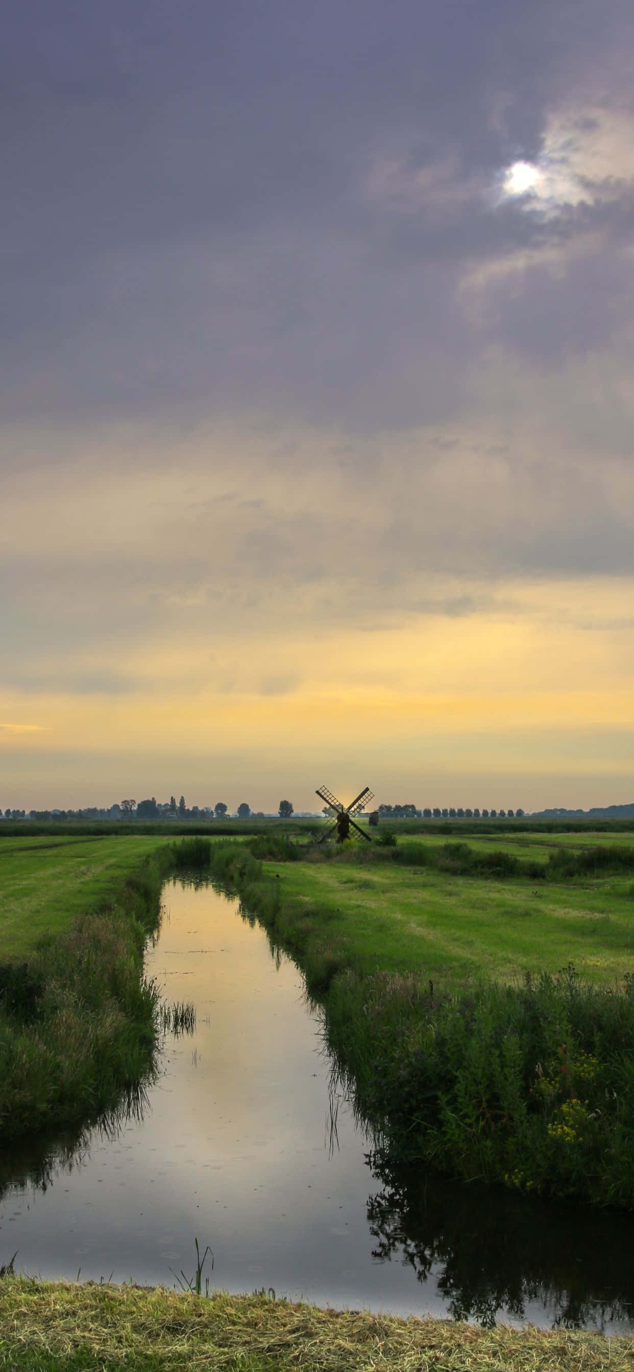 岩石峭壁與晶瑩藍水的海灘風景 壁紙 — 寧靜的黃昏場景，一座傳統風車矗立在平靜的運河旁，倒映著柔和的金色天空。