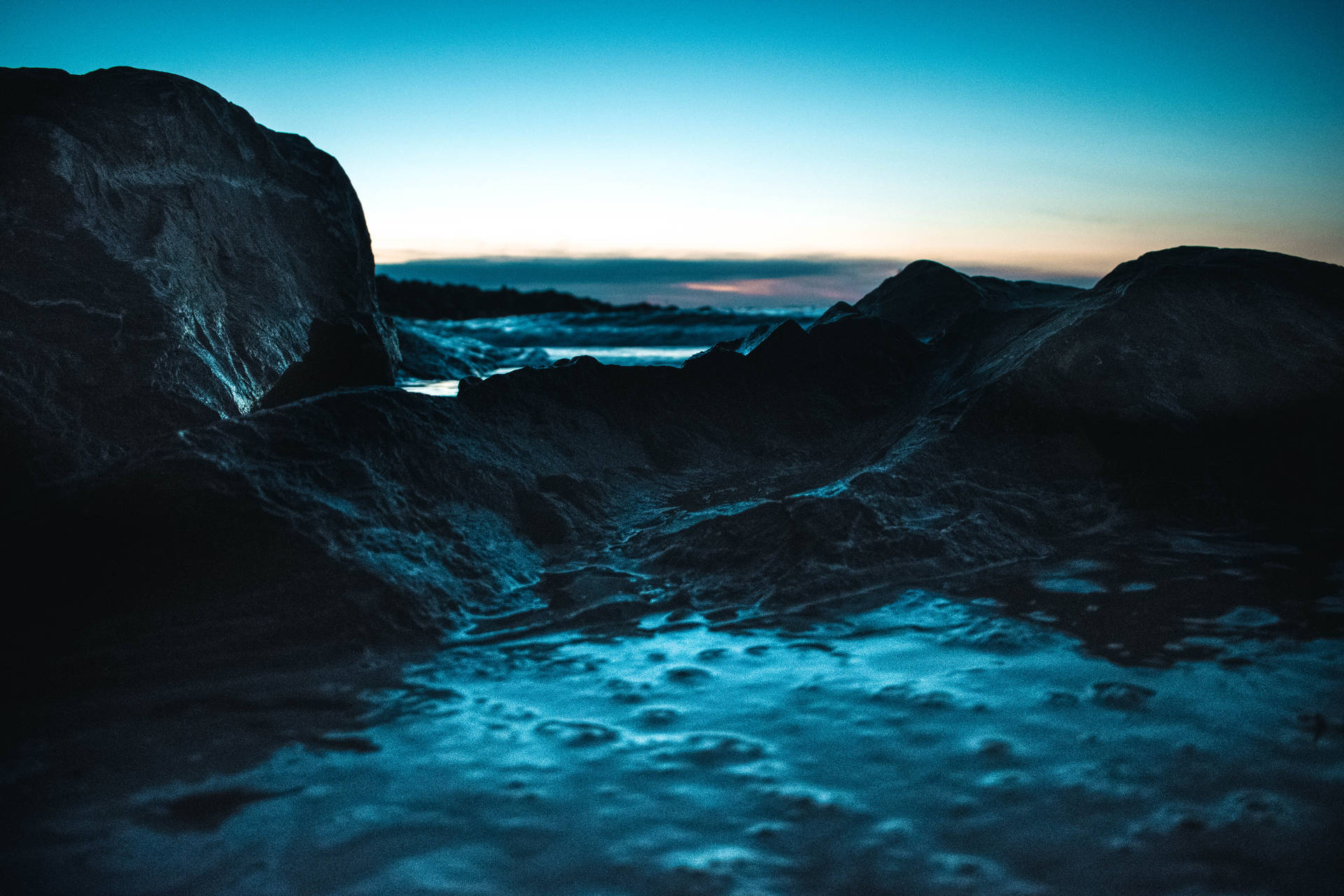 藍天下，黃昏海灘上的深色岩石和泡沫波浪。