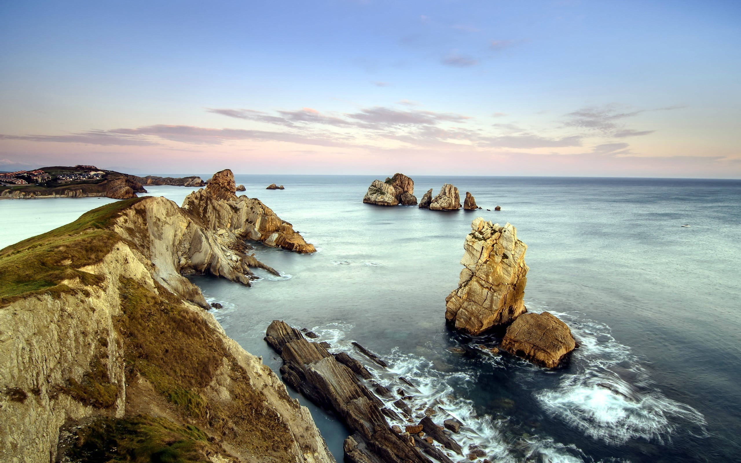 岩石海岸的寧靜晨光 壁紙 — 夕陽將戲劇性的海岸懸崖和海蝕柱沐浴在溫暖的光線中，海浪拍打著崎嶇的岩石。