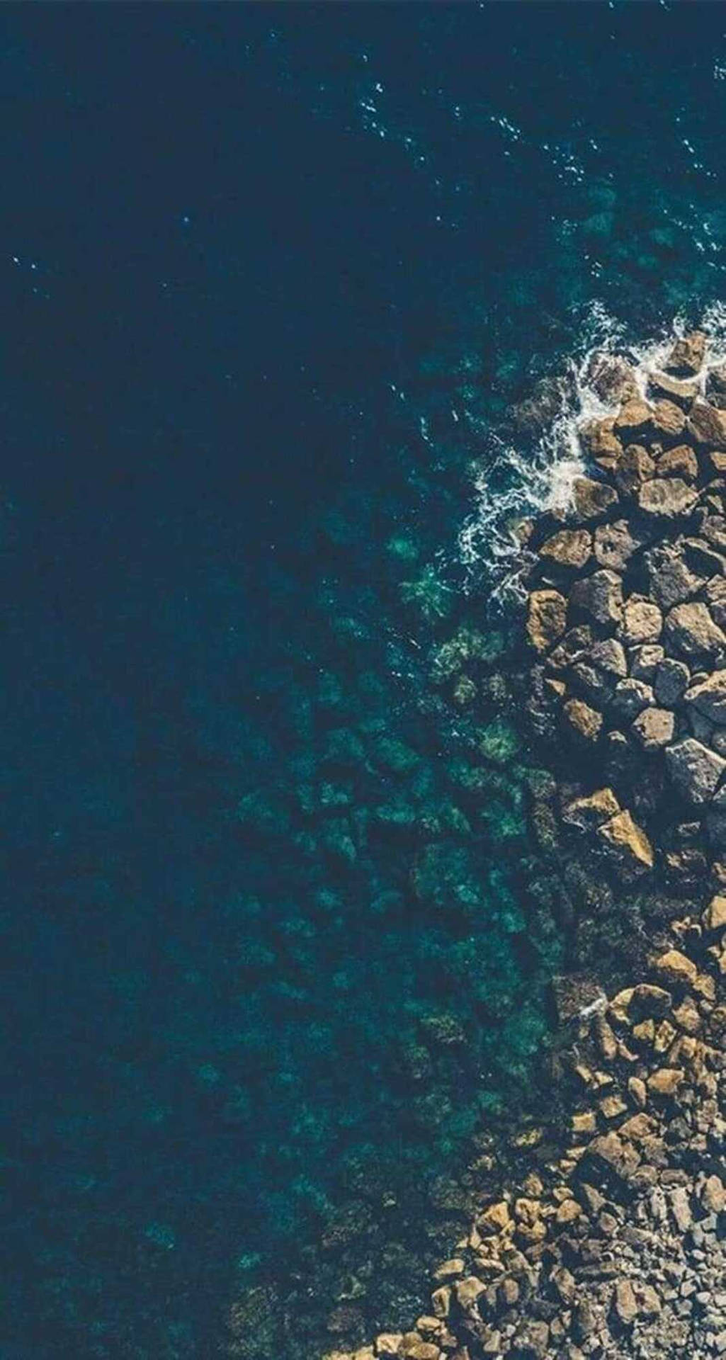 海浪拍打岩石海岸線，海水清澈碧綠。 — 主螢幕 壁紙
