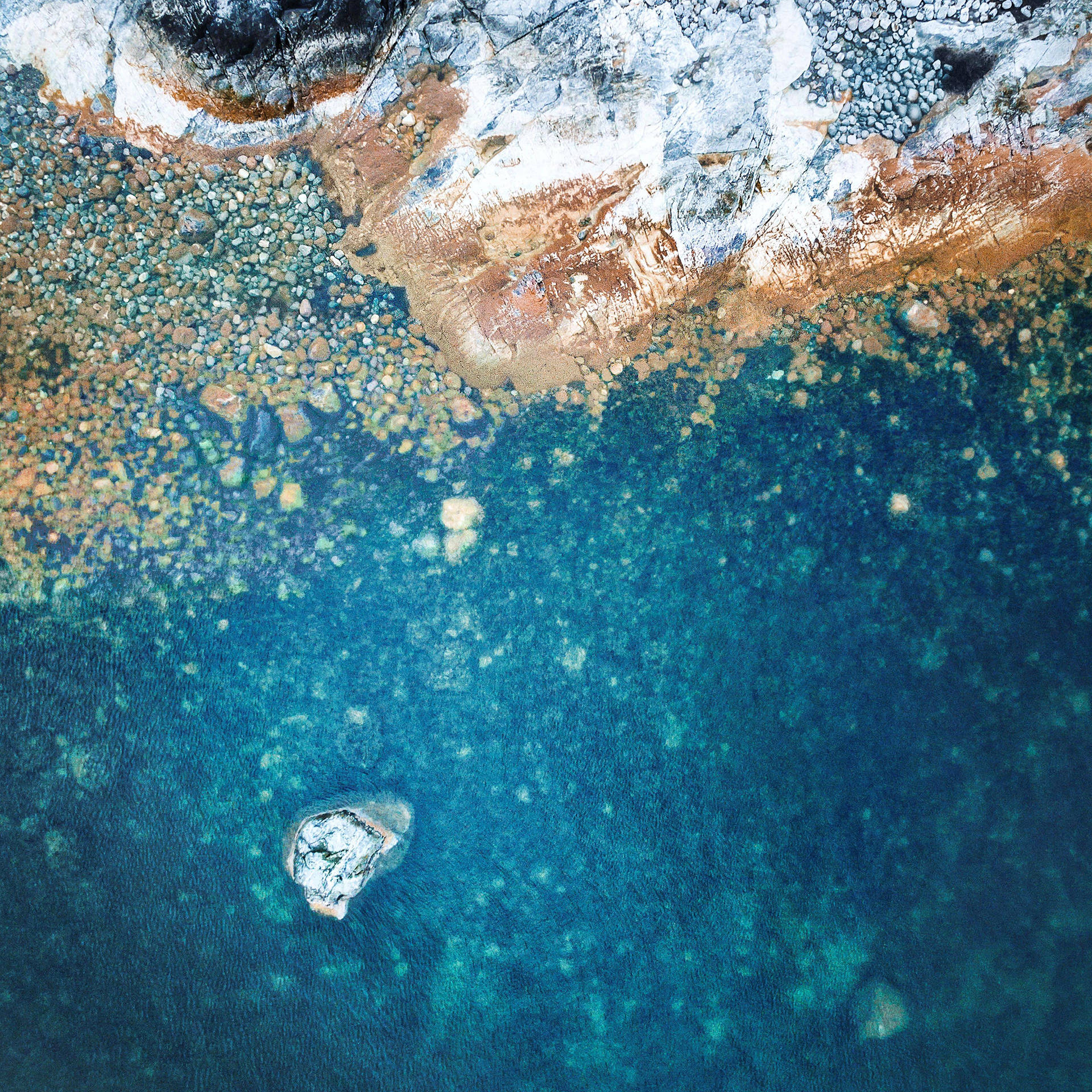 從高空俯瞰，碧綠的海水與岩石海岸交匯，散落著鵝卵石和一個小島。