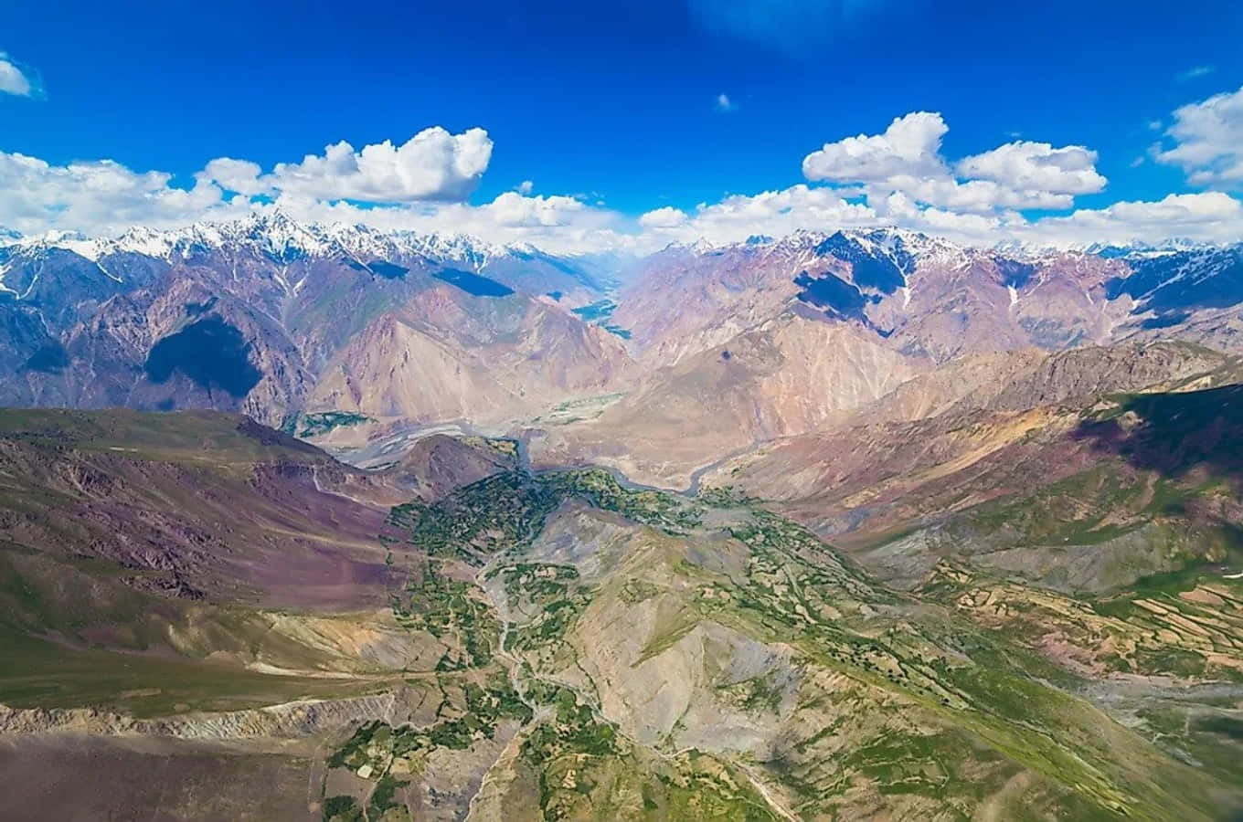 Afghanistan 桌布 壁紙 — 崎嶇山脈的鳥瞰圖，山峰積雪，在明亮的藍天下點綴著蓬鬆的白雲。