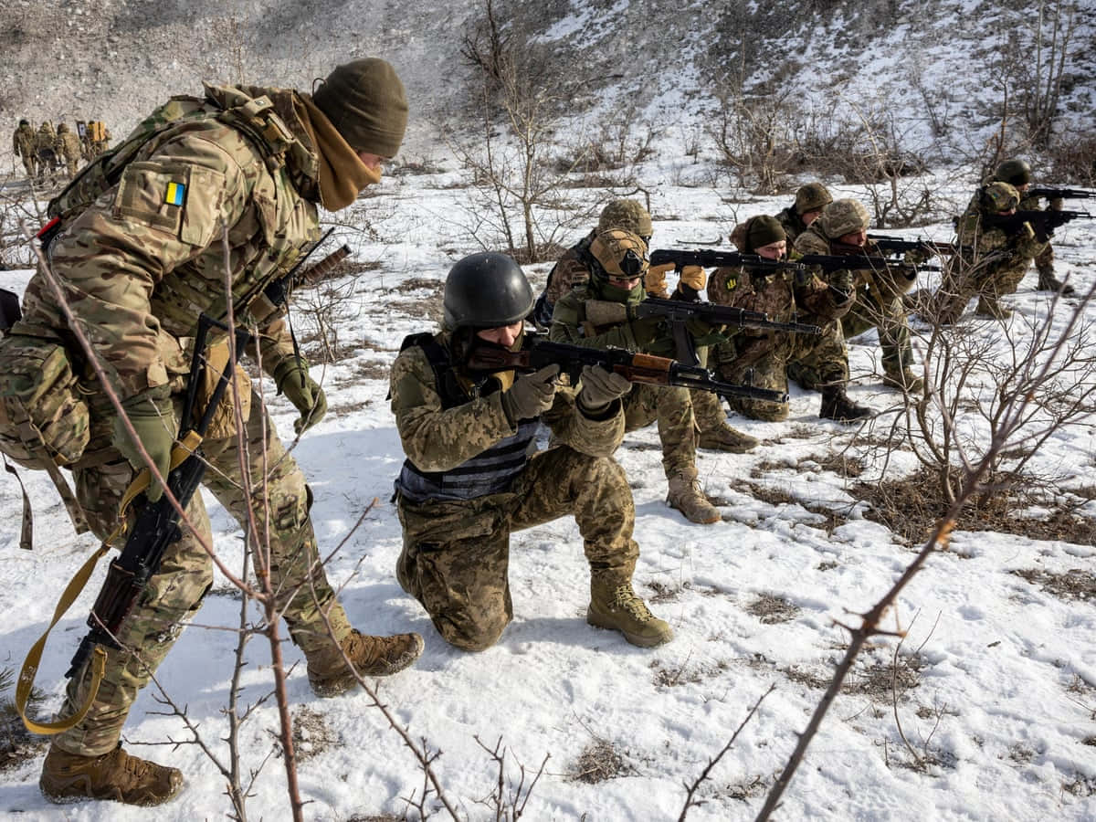 「崛起吧，永不放棄」 壁紙 — 穿著迷彩裝備的士兵在明亮的日光下，步槍指向前方，穿越雪地地形前進。